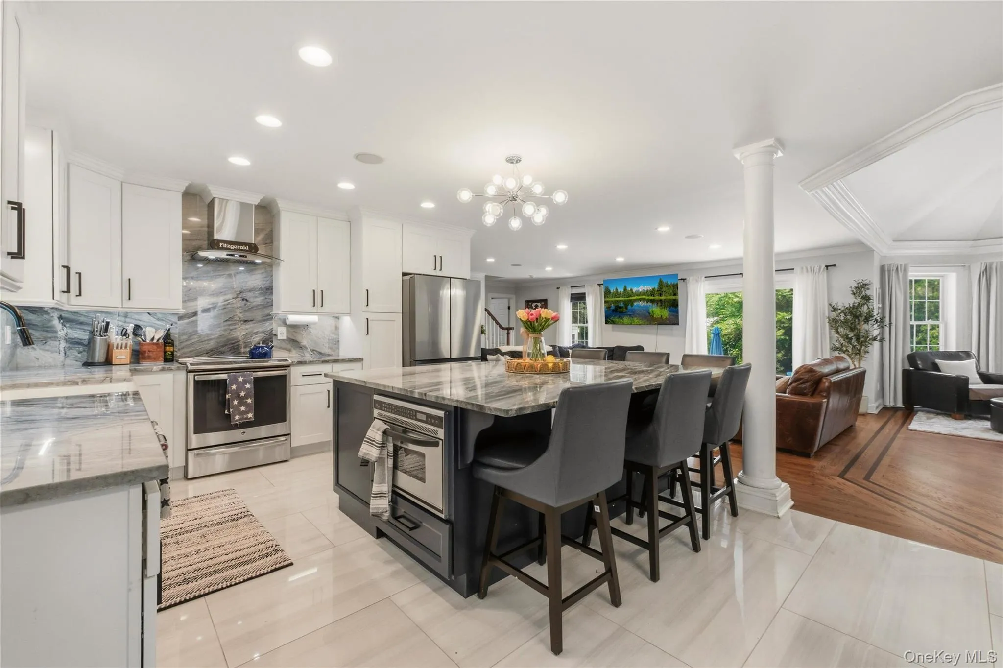 The heart of the home shines with this beautifully designed gourmet kitchen. A striking marble island with dramatic veining serves as the centerpiece, surrounded by sleek white cabinetry, stainless steel appliances, and a matching marble backsplash. Thoughtful details — from the contemporary chandelier to the decorative centerpiece — elevate the space with both style and practicality. The heart of the home shines with this beautifully designed gourmet kitchen. A striking marble island with dramatic veining serves as the centerpiece, surrounded by sleek white cabinetry, stainless steel appliances, and a matching marble backsplash. Thoughtful details — from the contemporary chandelier to the decorative centerpiece — elevate the space with both style and practicality.