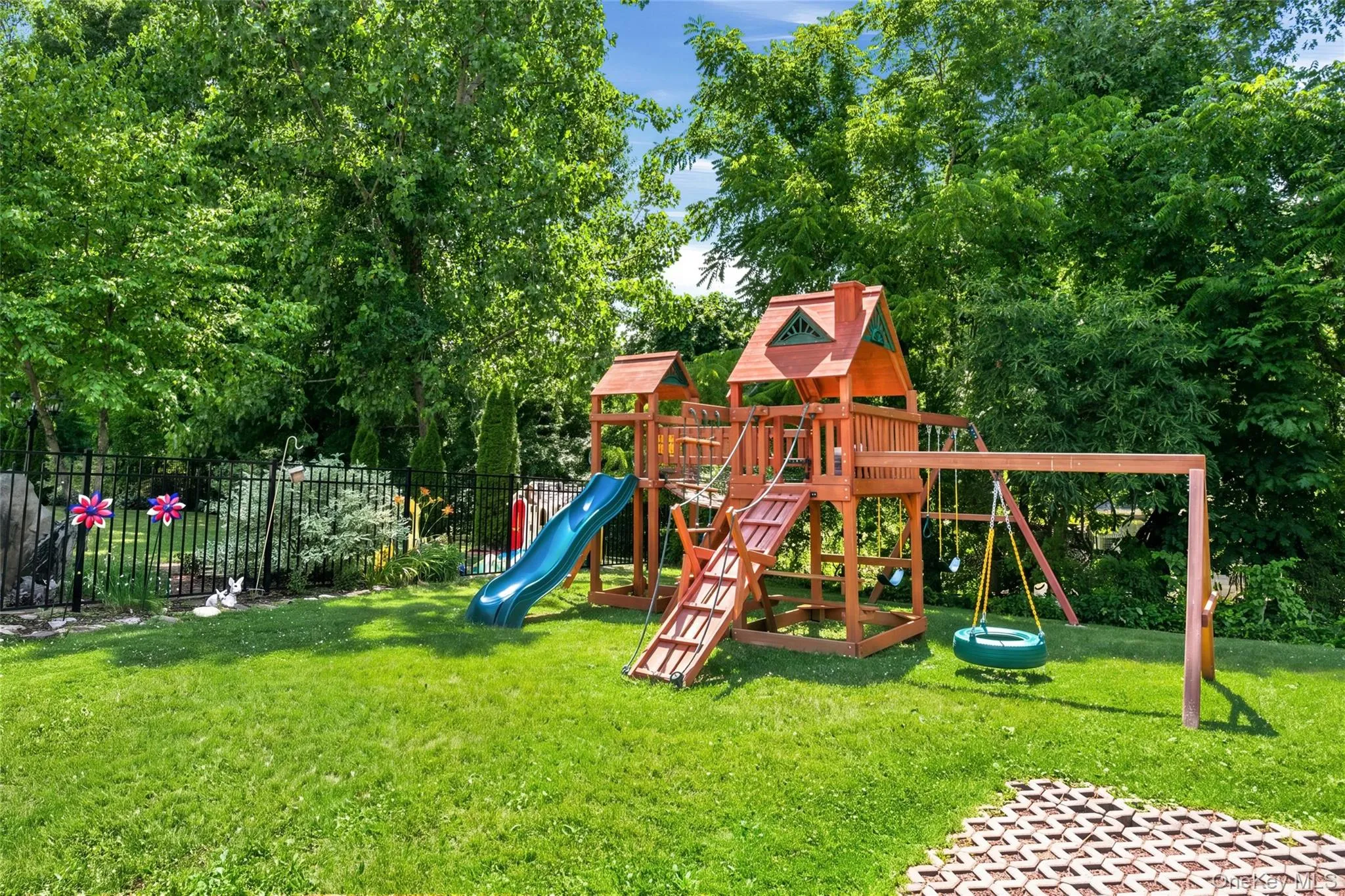 1 of 2 playgrounds on the property. This charming wooden playset offers swings, a slide, and climbing features surrounded by lush greenery. It’s a perfect outdoor space for children to explore and play. 1 of 2 playgrounds on the property. This charming wooden playset offers swings, a slide, and climbing features surrounded by lush greenery. It’s a perfect outdoor space for children to explore and play.