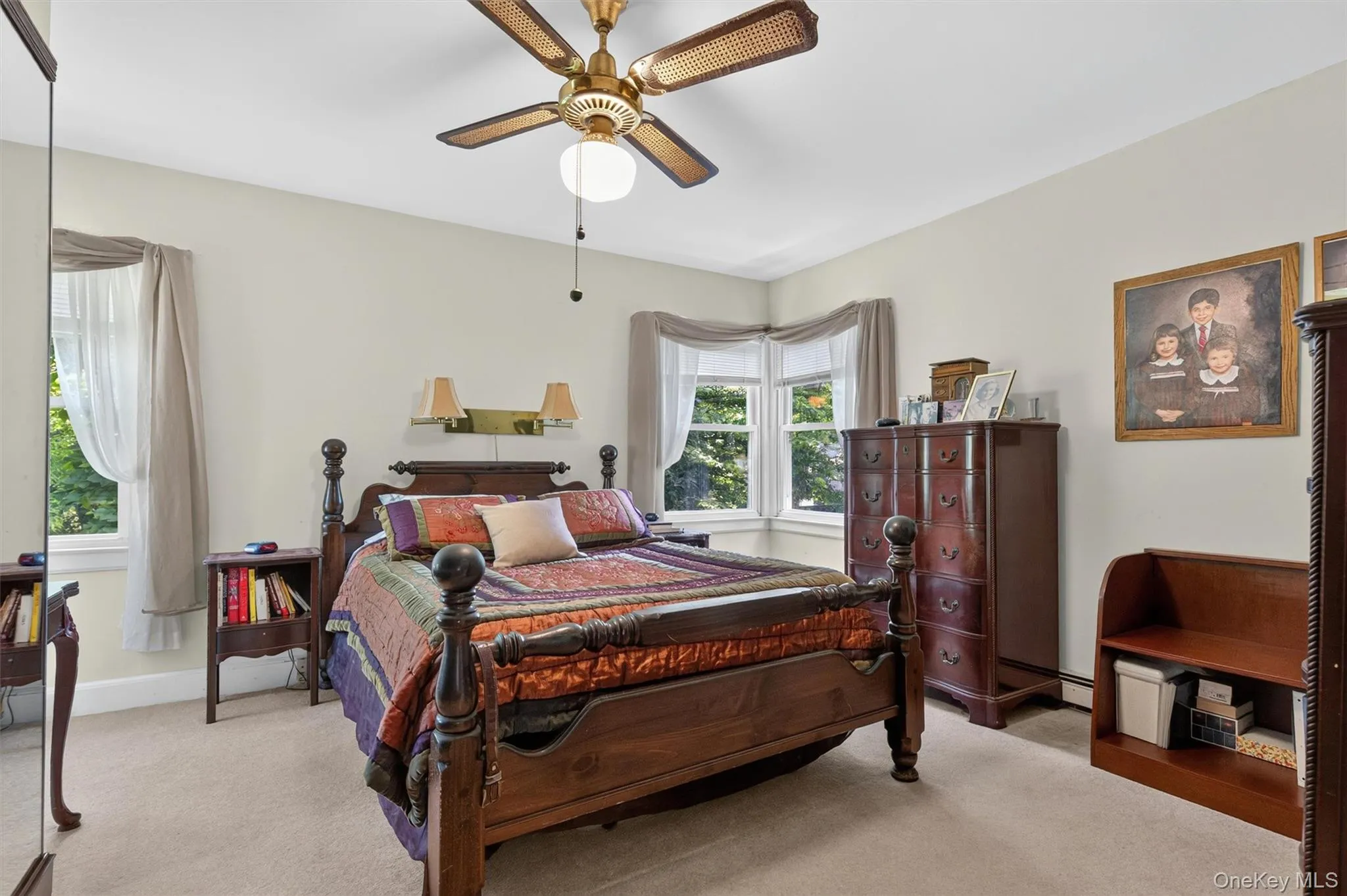 Carpeted bedroom featuring multiple windows with natural light, a ceiling fan with integrated lighting, and neutral wall tones Carpeted bedroom featuring multiple windows with natural light, a ceiling fan with integrated lighting, and neutral wall tones