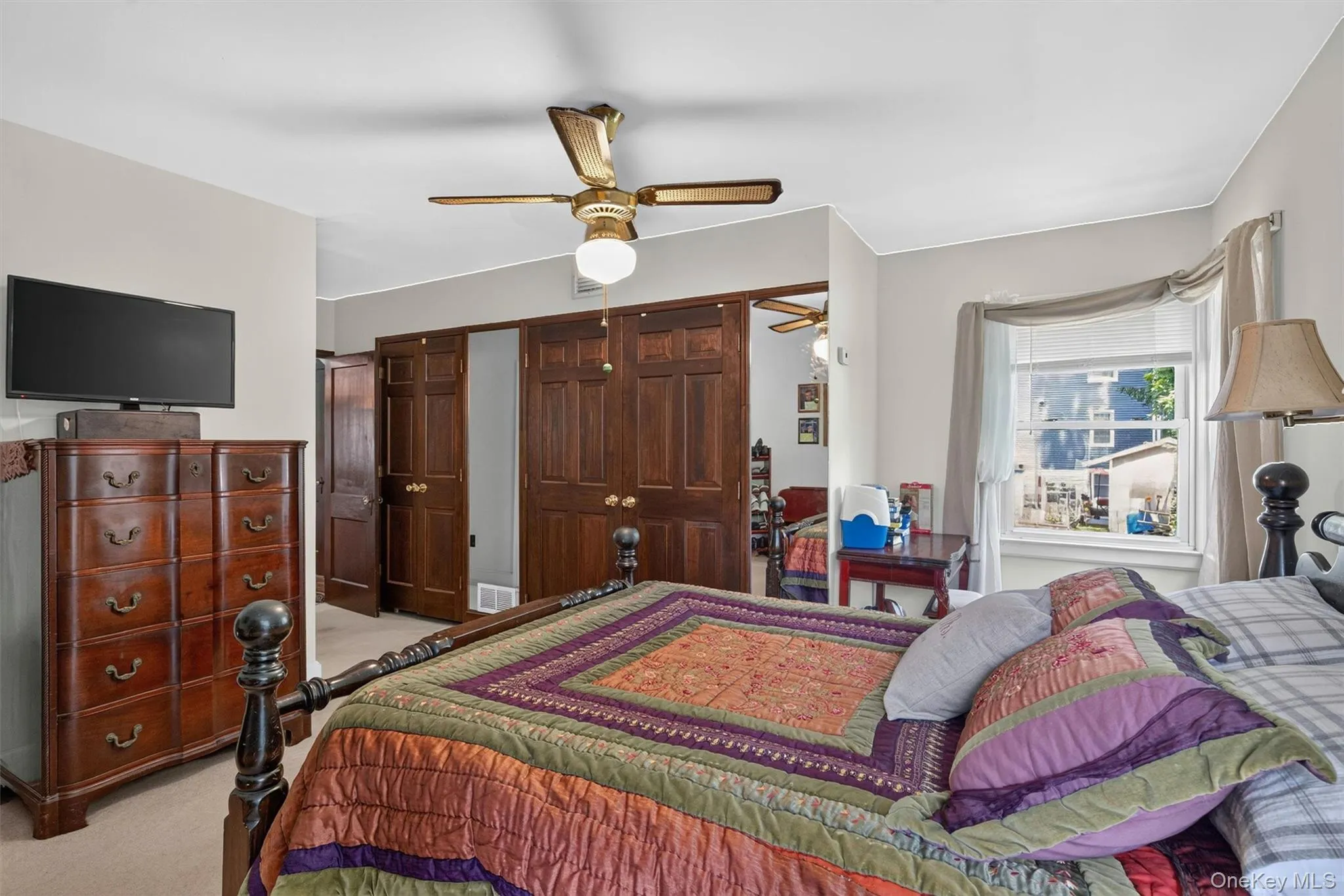 Bedroom featuring a ceiling fan with integrated lighting, wood-finish bi-fold closet doors, a single window with white trim, and light-colored wall paint Bedroom featuring a ceiling fan with integrated lighting, wood-finish bi-fold closet doors, a single window with white trim, and light-colored wall paint