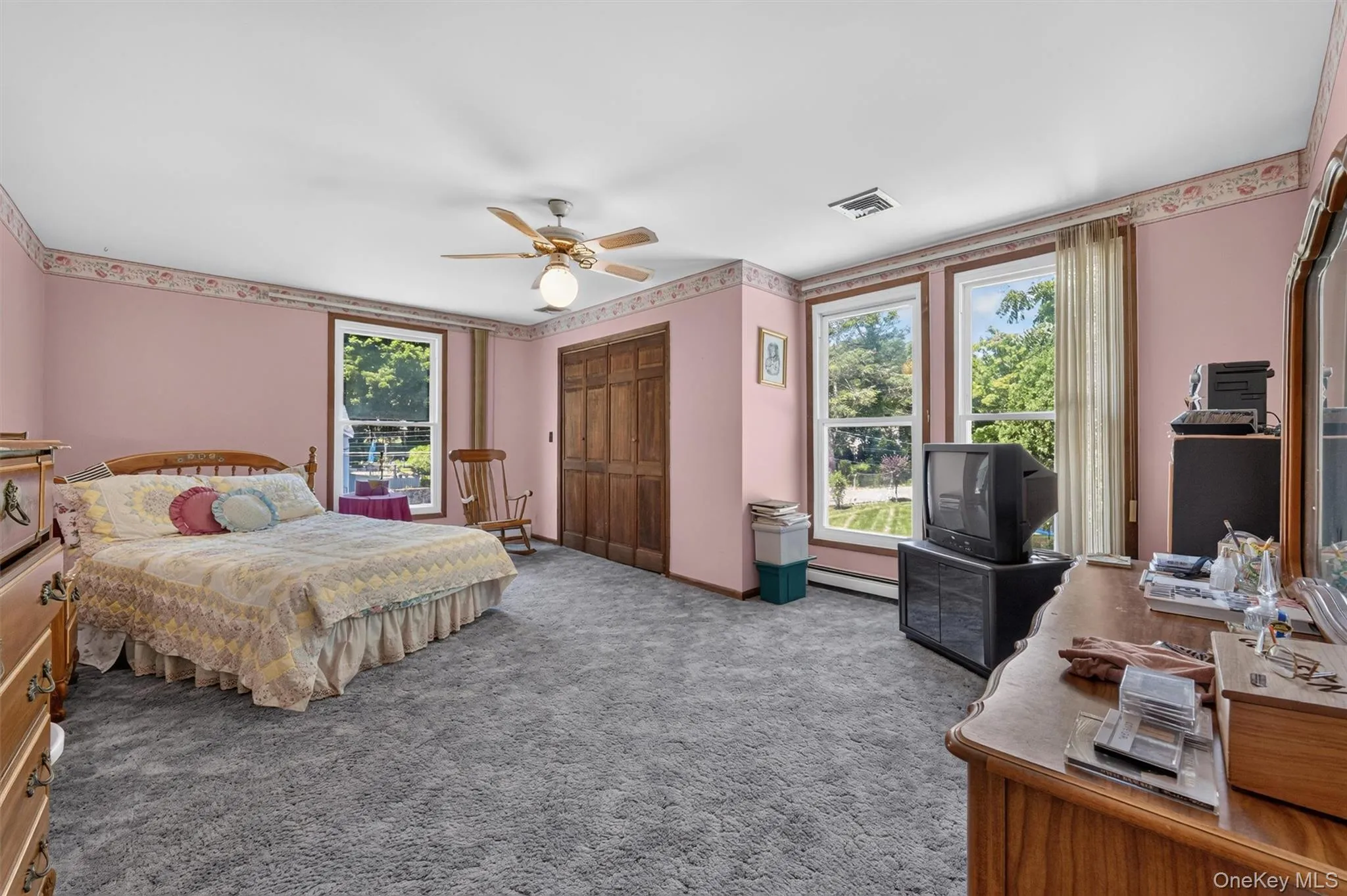 Spacious room featuring gray carpeting, three sash windows with white framing, and wood-finish bi-fold closet doors Spacious room featuring gray carpeting, three sash windows with white framing, and wood-finish bi-fold closet doors
