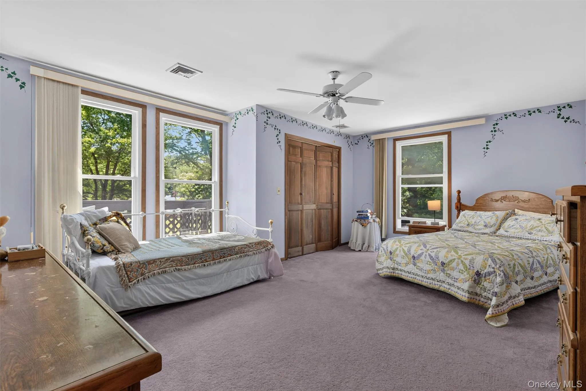 Spacious room featuring two large windows, wood-finish trim, a ceiling fan, plush carpeting, and built-in wood-finish closets Spacious room featuring two large windows, wood-finish trim, a ceiling fan, plush carpeting, and built-in wood-finish closets