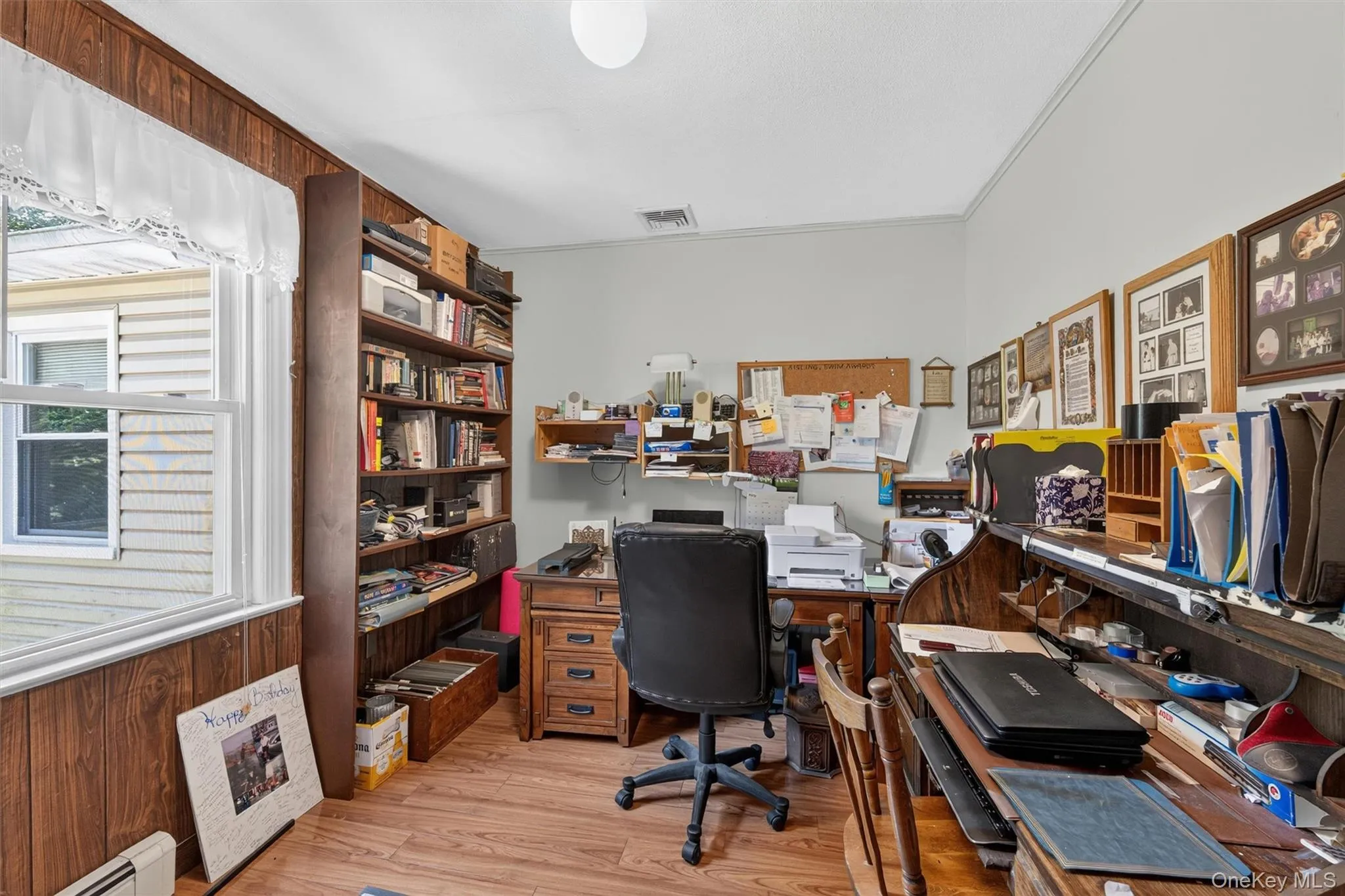 Interior room featuring wood-finish flooring, a built-in bookshelf, and wood paneling on one wall Interior room featuring wood-finish flooring, a built-in bookshelf, and wood paneling on one wall