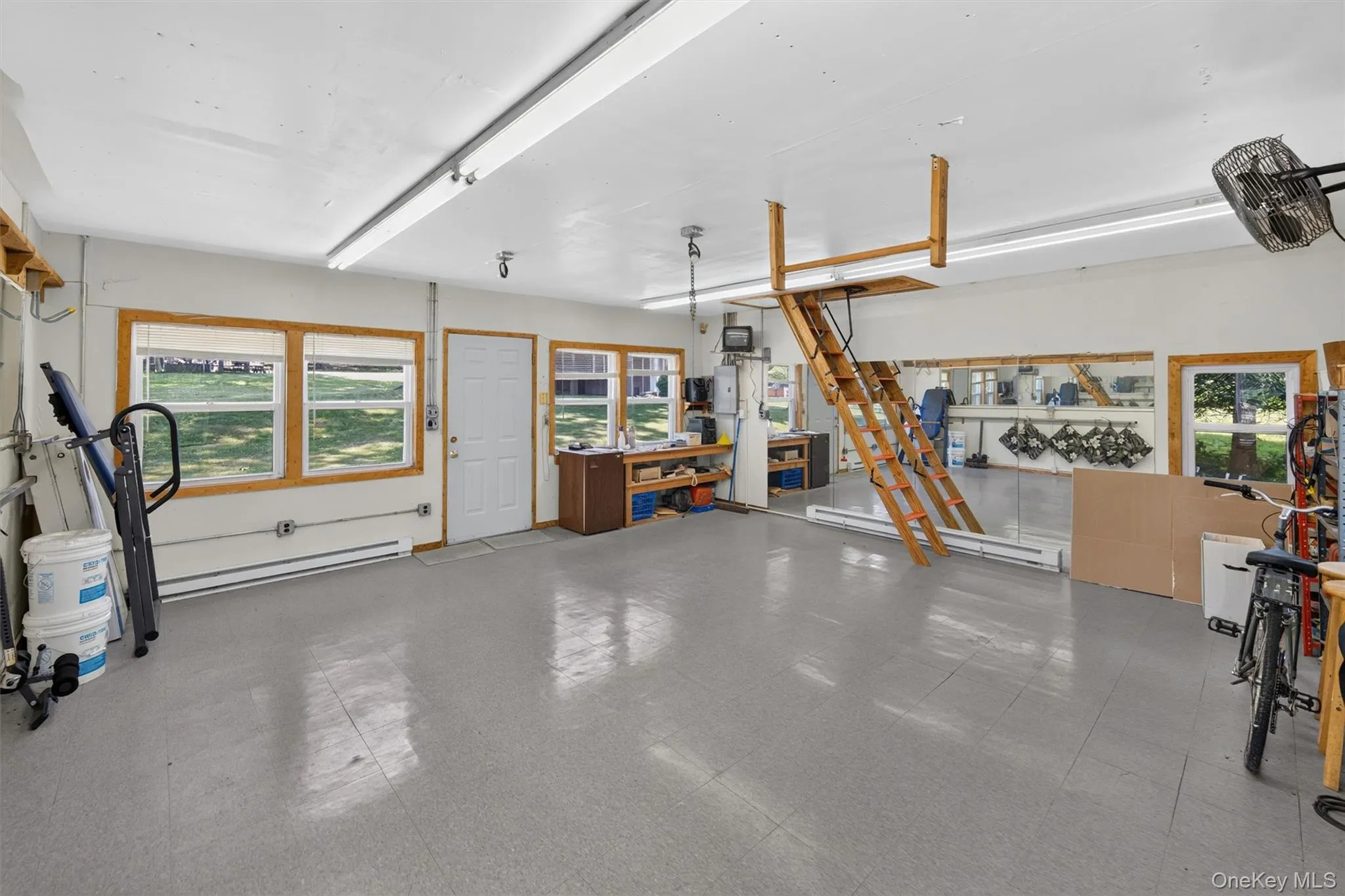 Spacious utility room featuring multiple windows with wood trim, grey flooring, and a white ceiling with fluorescent lighting Spacious utility room featuring multiple windows with wood trim, grey flooring, and a white ceiling with fluorescent lighting