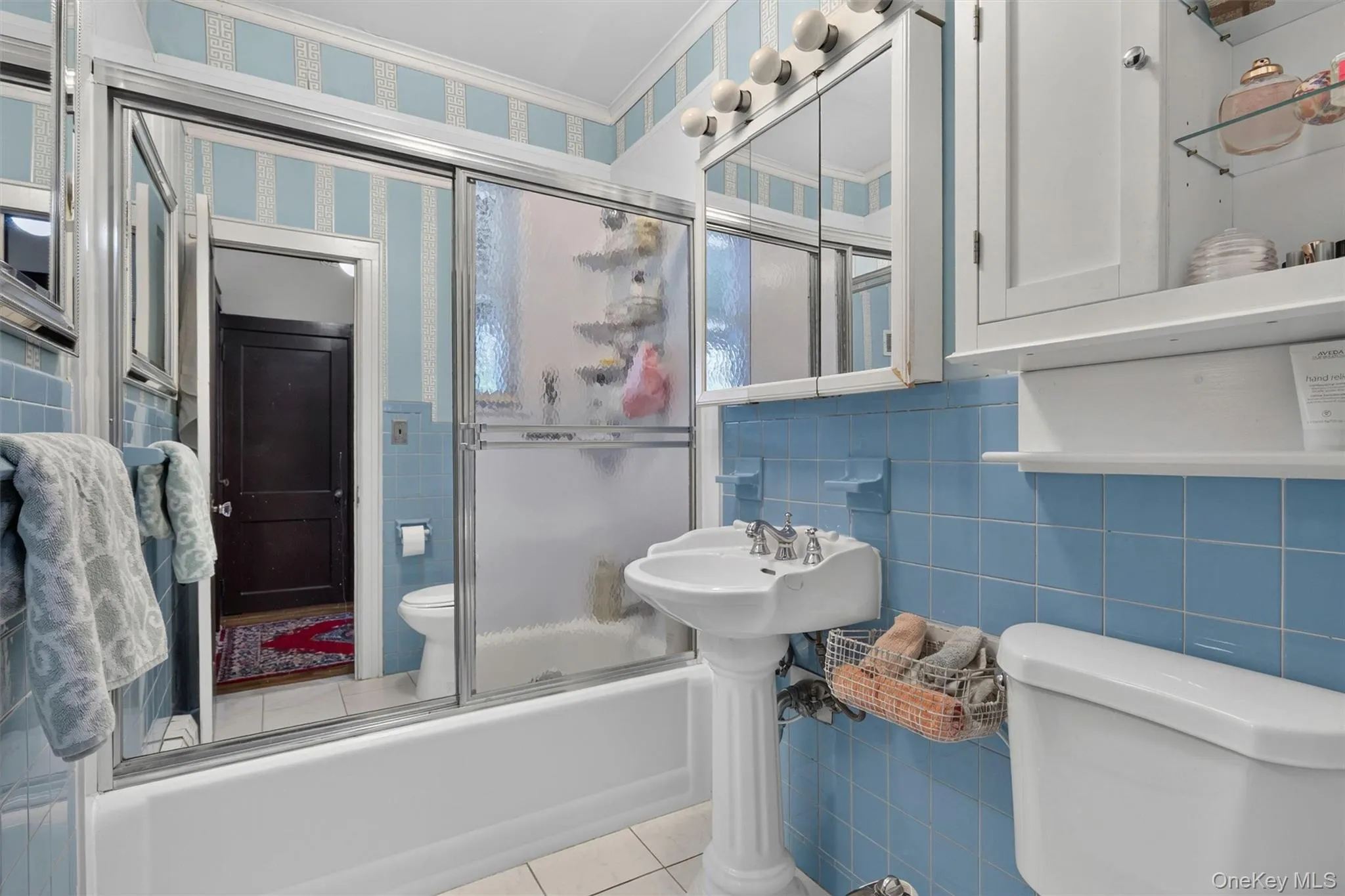 Bathroom featuring light blue wall tiles, a pedestal sink with a chrome faucet, and a shower-over-tub combination with sliding glass doors Bathroom featuring light blue wall tiles, a pedestal sink with a chrome faucet, and a shower-over-tub combination with sliding glass doors
