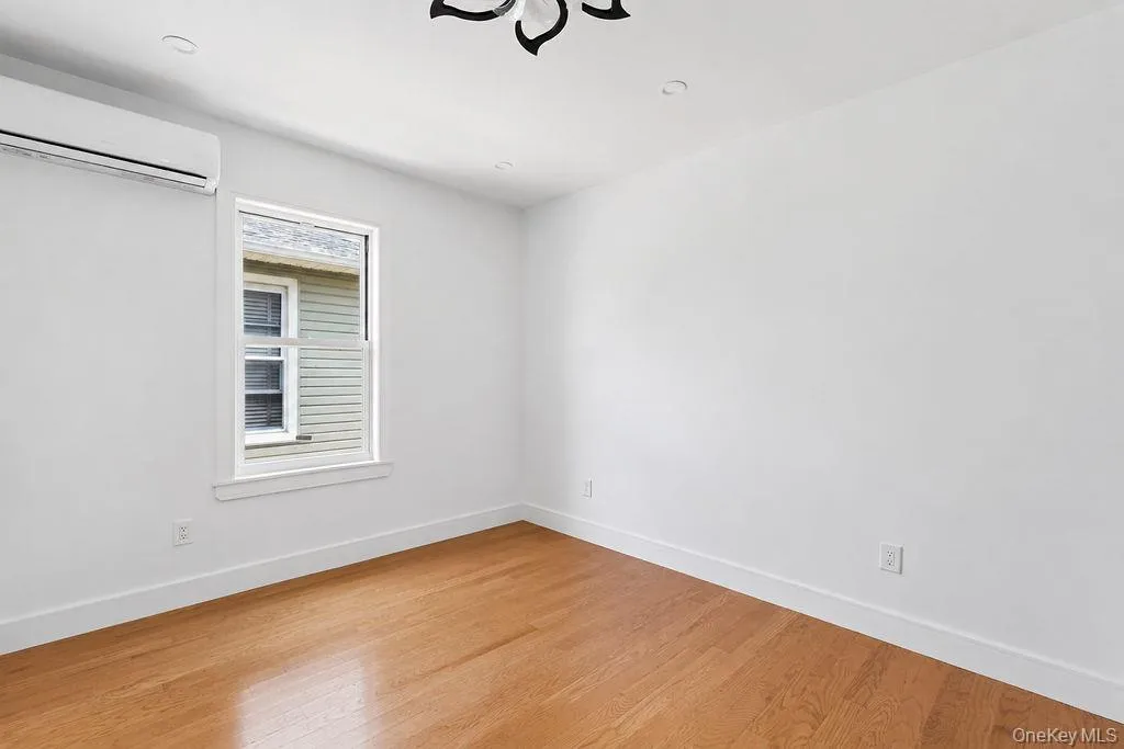 Hardwood flooring room with a single window, white walls, and a mini-split air conditioning unit Hardwood flooring room with a single window, white walls, and a mini-split air conditioning unit