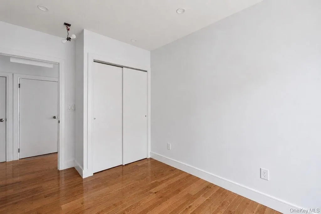 Bedroom featuring wood-finish flooring, white walls, and a built-in closet with sliding doors Bedroom featuring wood-finish flooring, white walls, and a built-in closet with sliding doors