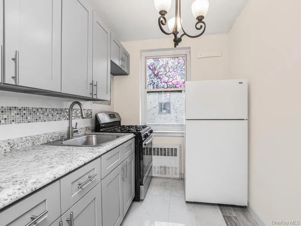Kitchen with freestanding refrigerator, stainless steel range with gas stovetop, gray cabinetry, radiator, and backsplash Kitchen with freestanding refrigerator, stainless steel range with gas stovetop, gray cabinetry, radiator, and backsplash