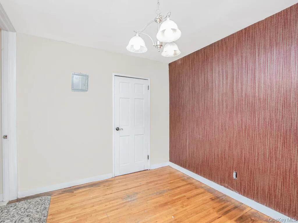 Unfurnished room with light wood-style floors, a chandelier, wood walls, and electric panel Unfurnished room with light wood-style floors, a chandelier, wood walls, and electric panel