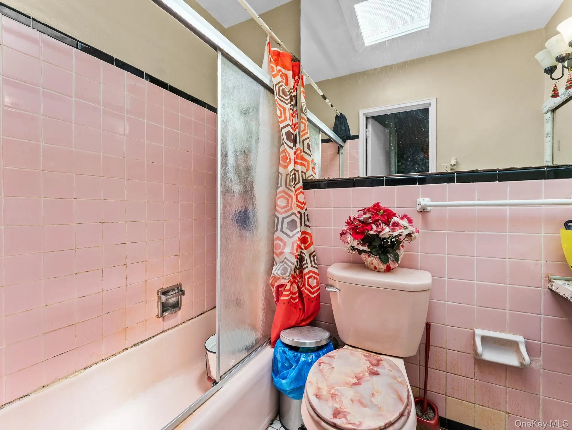 Bathroom 1st. Floor, featuring a bathtub with a sliding glass enclosure, pink wall tiling, and a skylight Bathroom 1st. Floor, featuring a bathtub with a sliding glass enclosure, pink wall tiling, and a skylight