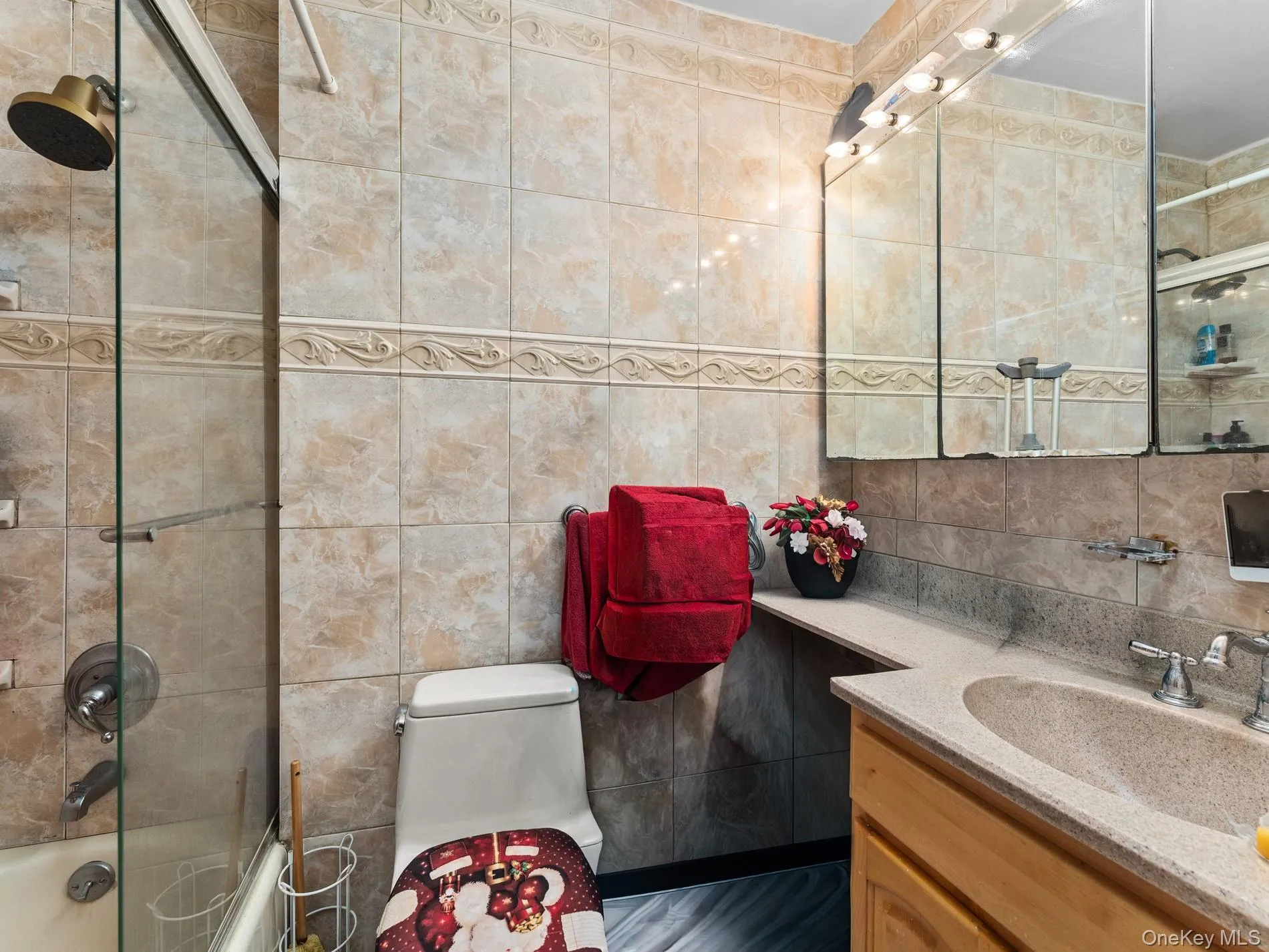 2nd Floor, Bathroom featuring stone-finish wall tiling with decorative trim, a shower-tub combination with a glass enclosure, a vanity with a built-in sink, a light wood-finish cabinet, and a multi-mirror medicine cabinet with integrated lighting 2nd Floor, Bathroom featuring stone-finish wall tiling with decorative trim, a shower-tub combination with a glass enclosure, a vanity with a built-in sink, a light wood-finish cabinet, and a multi-mirror medicine cabinet with integrated lighting