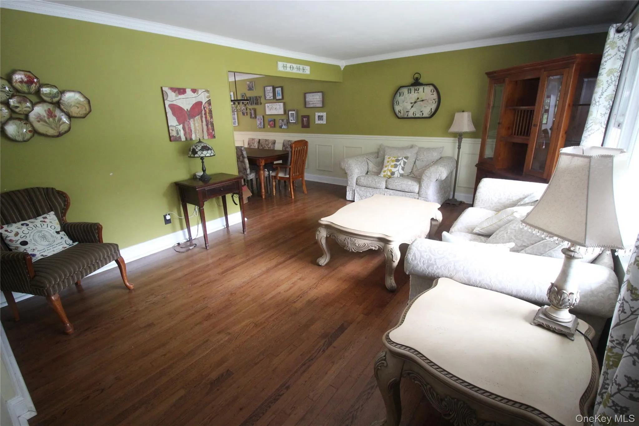 Expansive living area featuring rich wood-finish flooring, white crown molding, and wainscoting Expansive living area featuring rich wood-finish flooring, white crown molding, and wainscoting