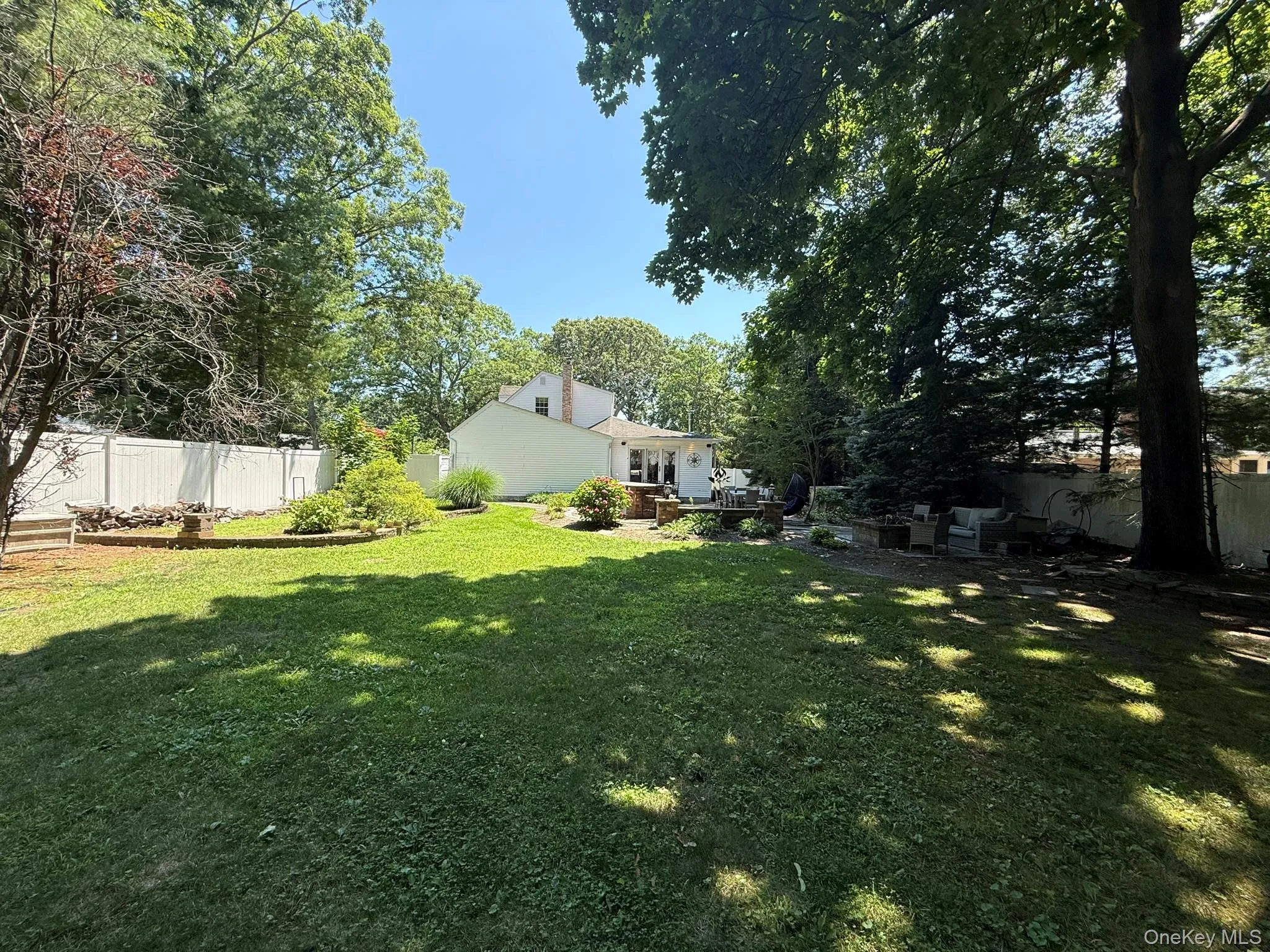 Expansive backyard featuring a lush lawn, white privacy fencing, and mature trees providing natural shade Expansive backyard featuring a lush lawn, white privacy fencing, and mature trees providing natural shade