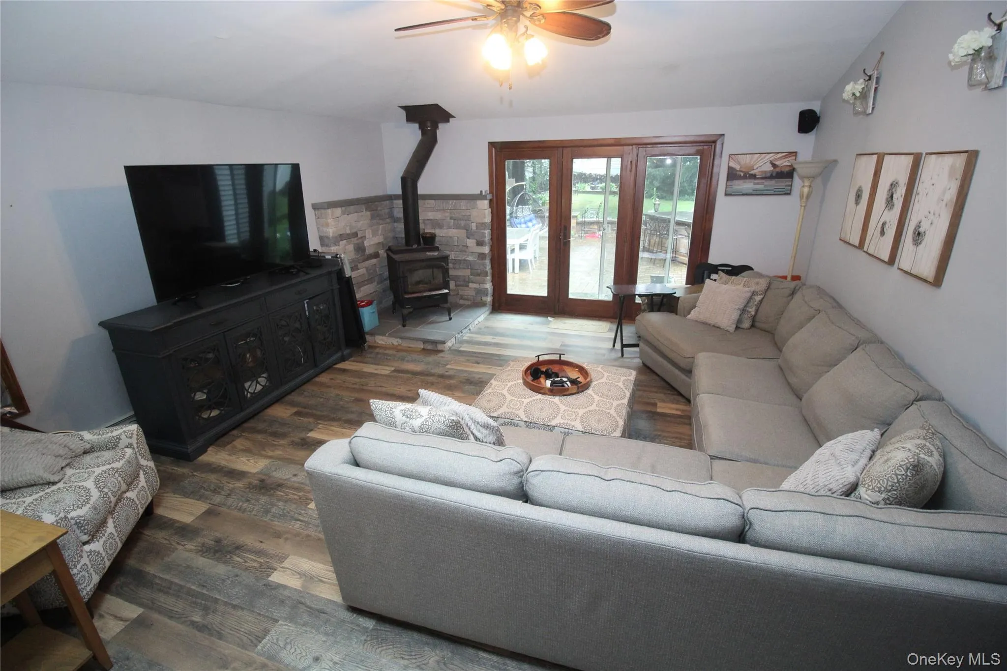 Living area featuring wood-finish flooring, a stone-accented wall with a wood-burning stove, and double glass French doors Living area featuring wood-finish flooring, a stone-accented wall with a wood-burning stove, and double glass French doors