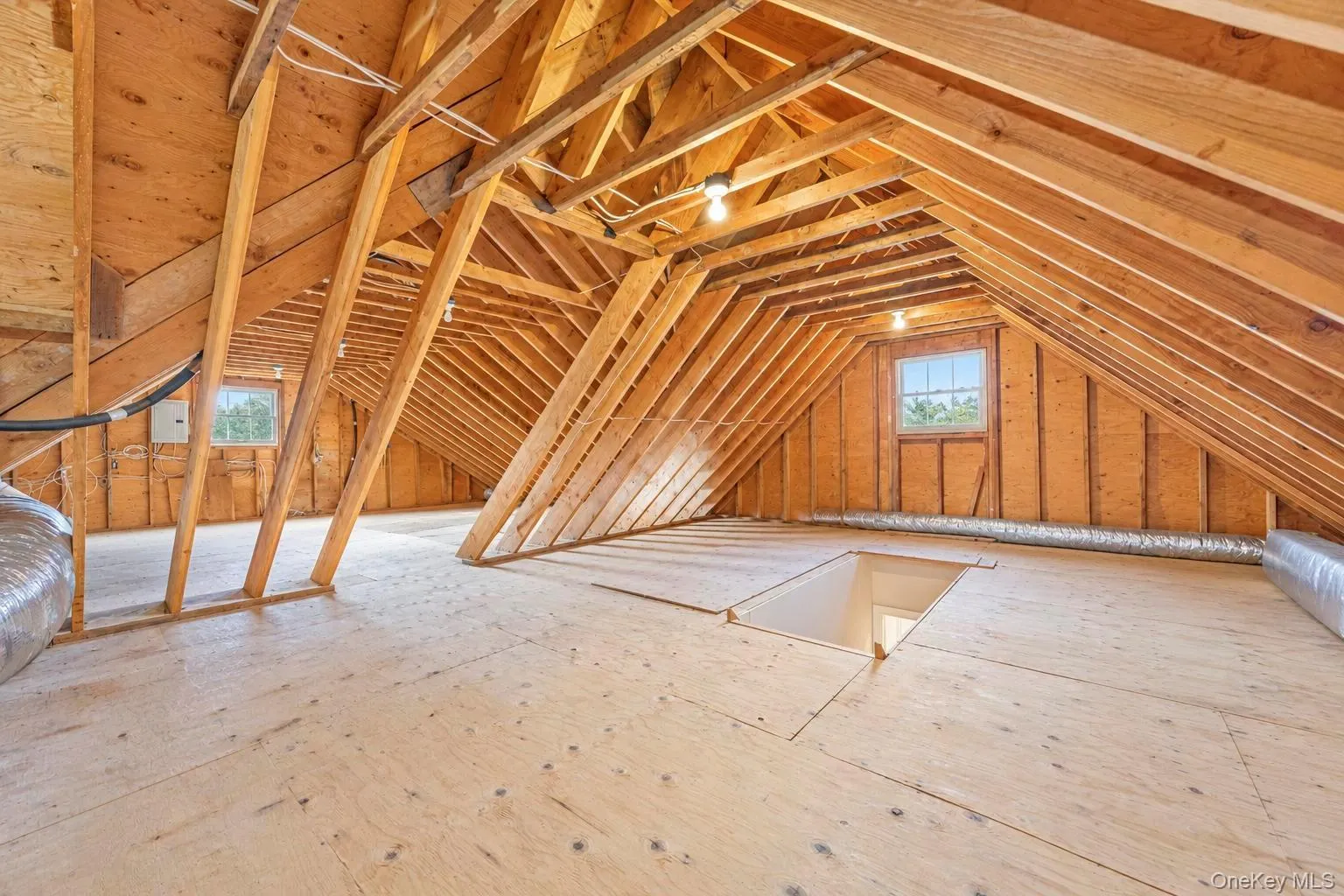 Open attic space with exposed wood rafters, plywood subflooring, and two operable windows Open attic space with exposed wood rafters, plywood subflooring, and two operable windows