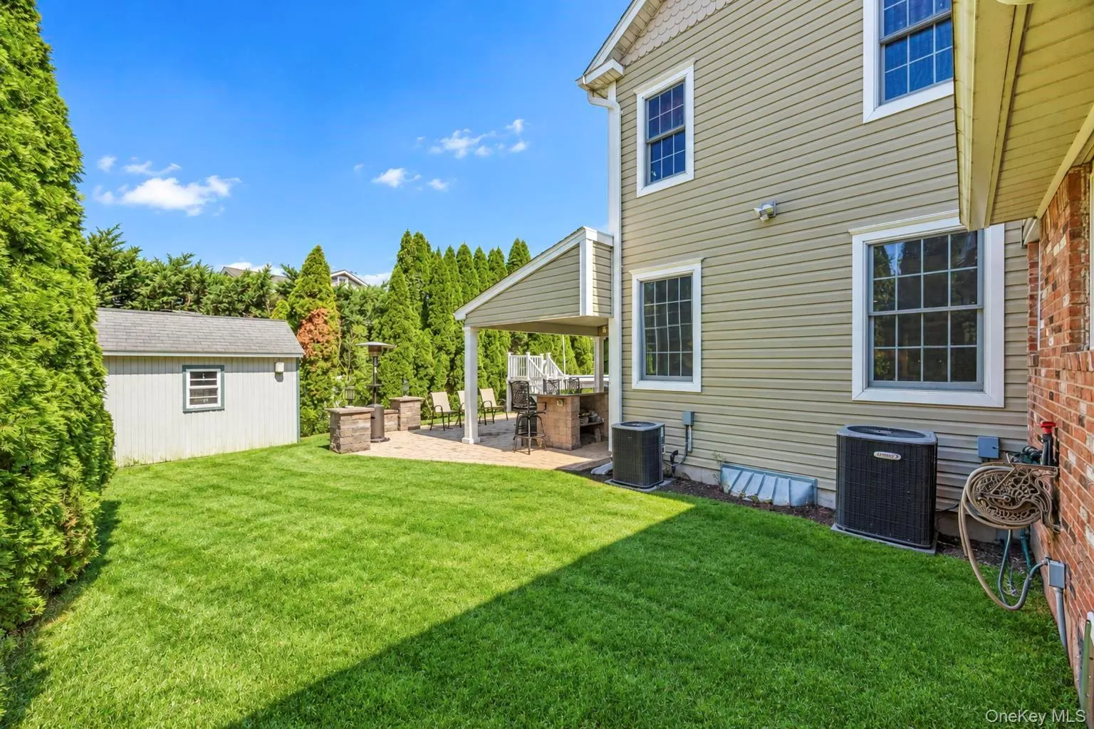 Expansive green lawn with a paver patio featuring a covered outdoor patio, a storage shed, and mature privacy plantings Expansive green lawn with a paver patio featuring a covered outdoor patio, a storage shed, and mature privacy plantings