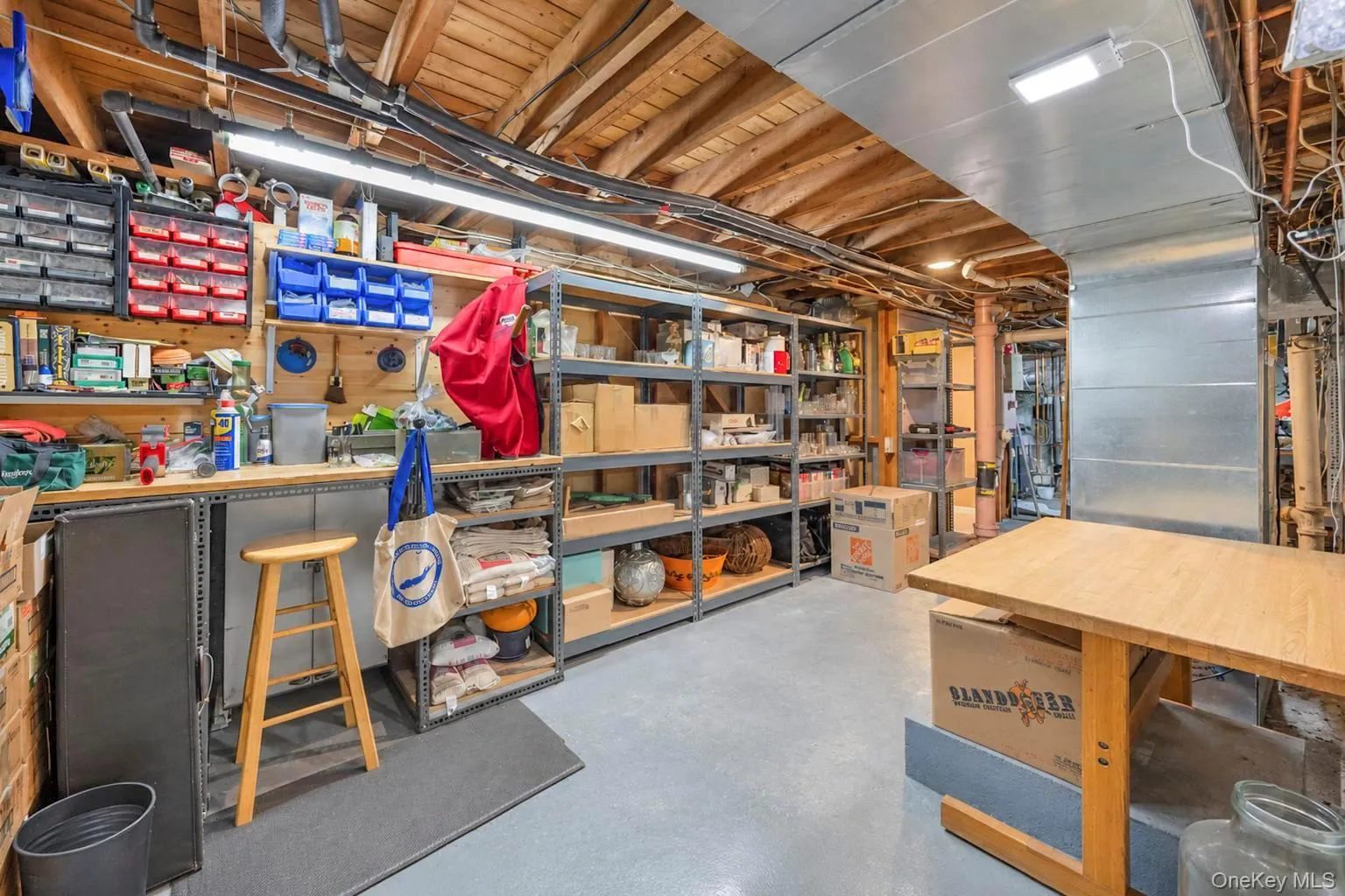 Utility space with exposed wood ceiling beams, overhead lighting, concrete flooring, and extensive metal shelving Utility space with exposed wood ceiling beams, overhead lighting, concrete flooring, and extensive metal shelving