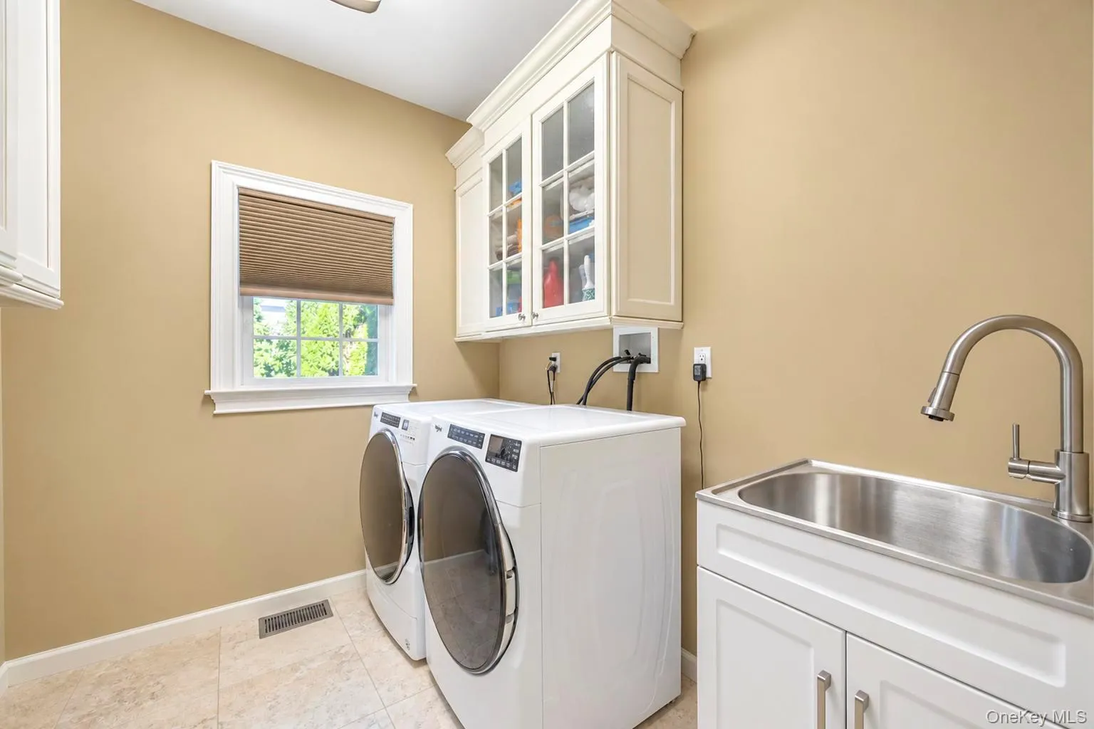 Laundry area featuring a utility sink with a pull-down faucet, white cabinetry with glass inserts, and tiled flooring Laundry area featuring a utility sink with a pull-down faucet, white cabinetry with glass inserts, and tiled flooring
