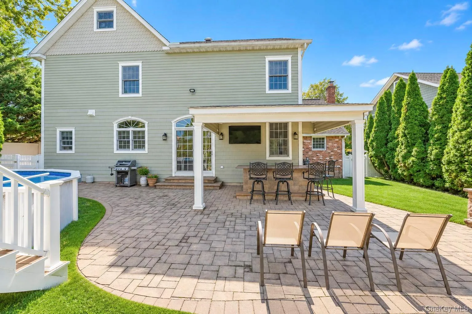 Expansive paver patio with covered outdoor bar, built-in entertainment, and a manicured lawn Expansive paver patio with covered outdoor bar, built-in entertainment, and a manicured lawn