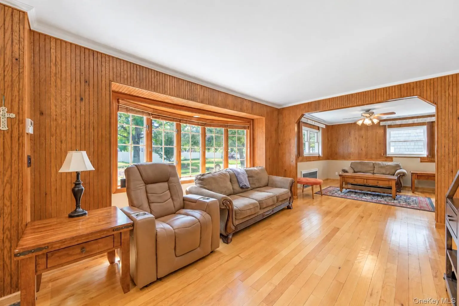 Hardwood flooring throughout, wood-paneled walls, a bay window with natural light, and a ceiling fan in the recessed area Hardwood flooring throughout, wood-paneled walls, a bay window with natural light, and a ceiling fan in the recessed area