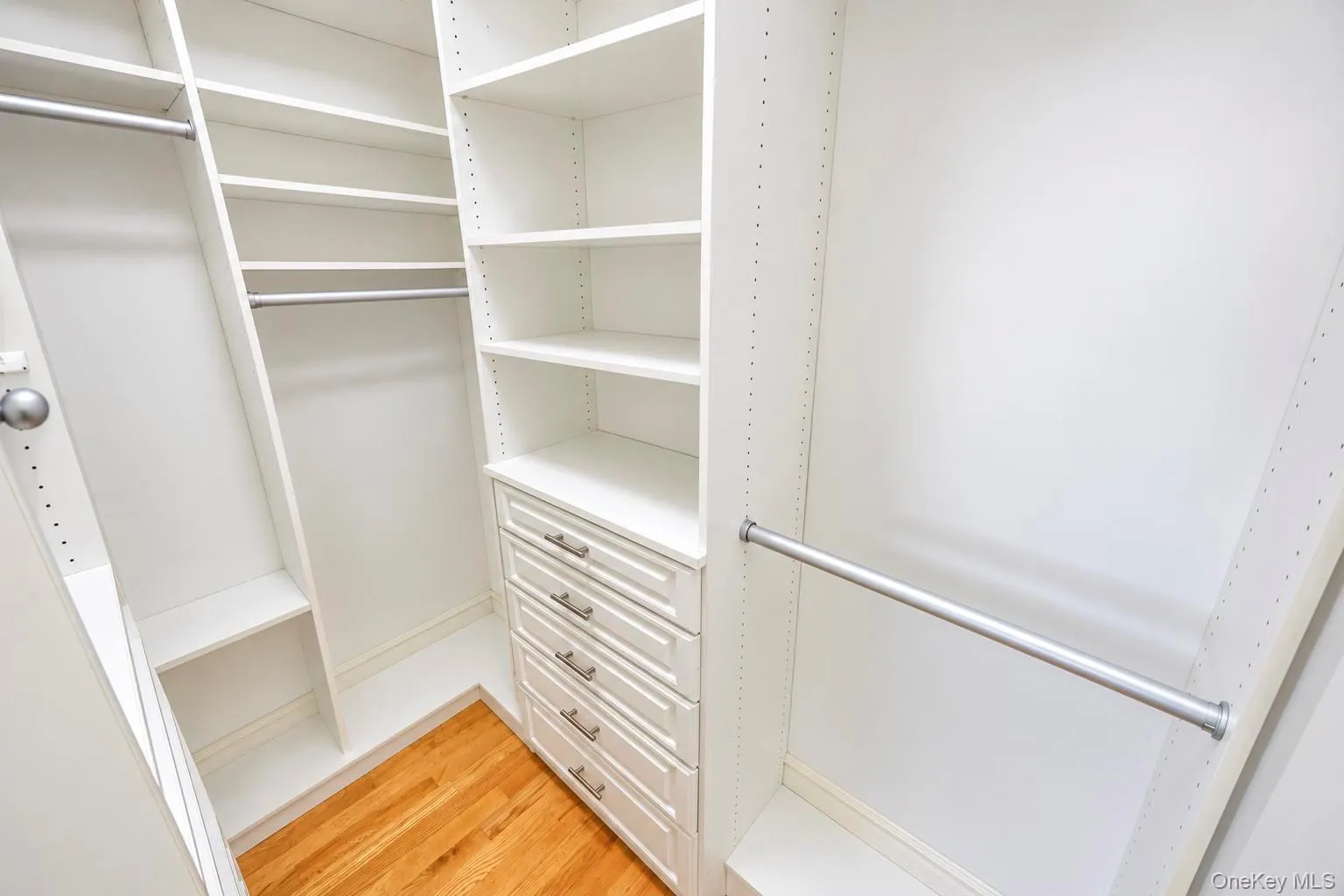 Custom closet system featuring white shelving, multiple hanging rods, and built-in drawers with brushed nickel hardware Custom closet system featuring white shelving, multiple hanging rods, and built-in drawers with brushed nickel hardware