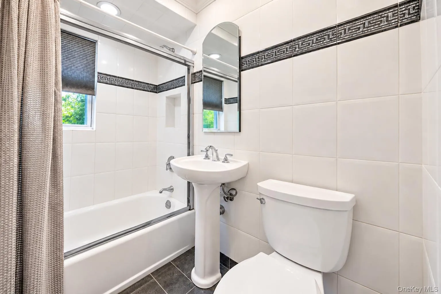 White tile walls featuring a decorative border, pedestal sink, and a built-in bathtub with a glass enclosure White tile walls featuring a decorative border, pedestal sink, and a built-in bathtub with a glass enclosure