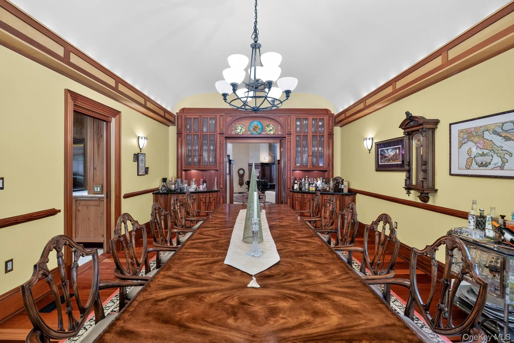 Formal dining room featuring wood-finish flooring, an ornate chandelier, and custom built-in cabinetry with glass doors Formal dining room featuring wood-finish flooring, an ornate chandelier, and custom built-in cabinetry with glass doors
