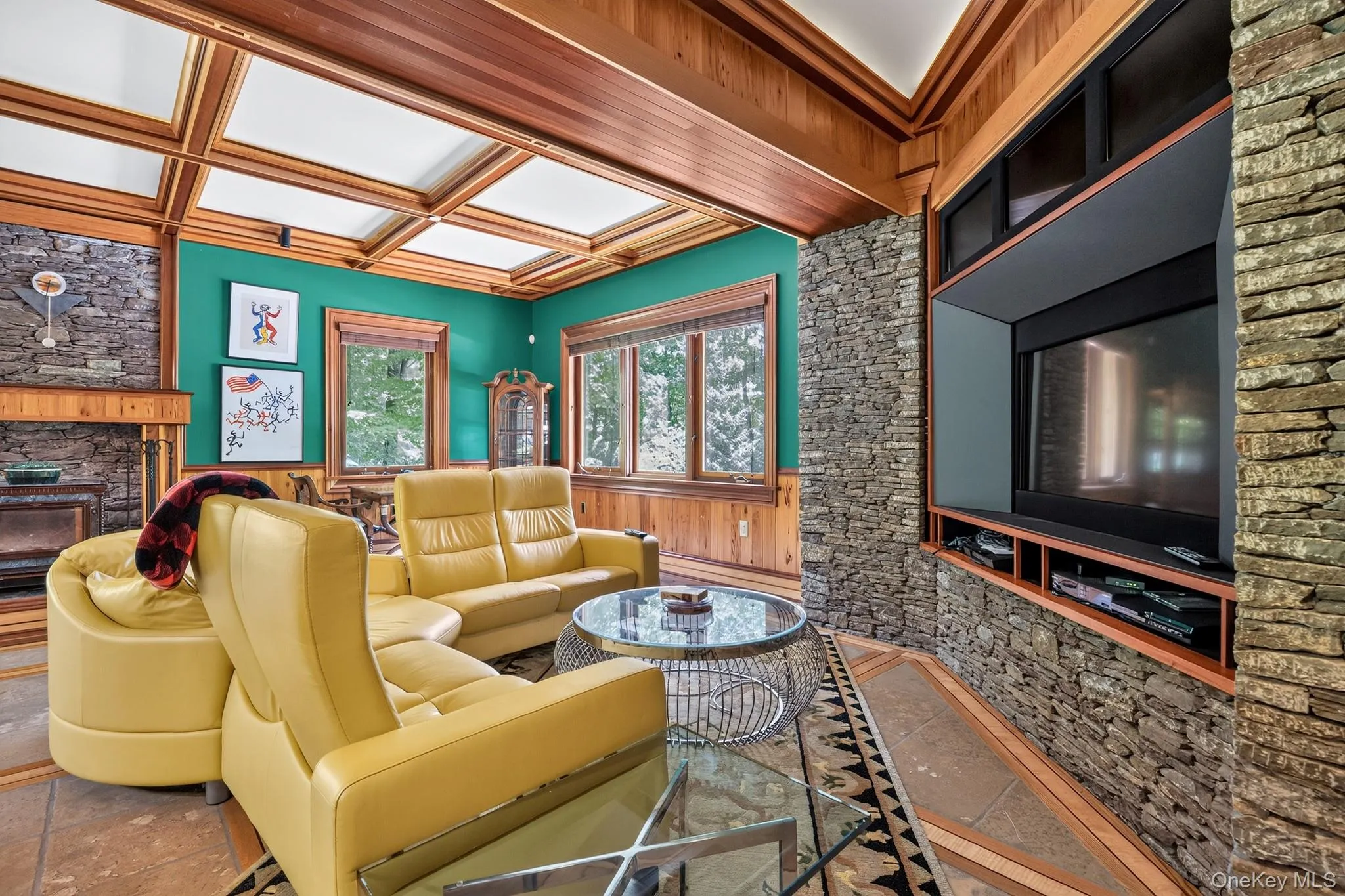Living area featuring a coffered wood-panel ceiling, stone-clad fireplace with a wood mantel, and built-in media center with stone surround Living area featuring a coffered wood-panel ceiling, stone-clad fireplace with a wood mantel, and built-in media center with stone surround