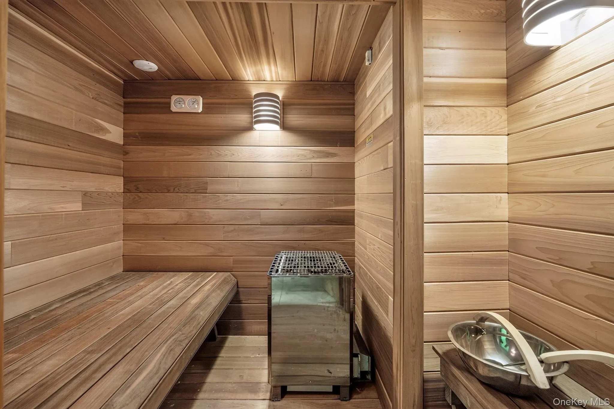 Sauna room featuring full wood-paneling, built-in wooden benches, and a wall-mounted heater unit Sauna room featuring full wood-paneling, built-in wooden benches, and a wall-mounted heater unit