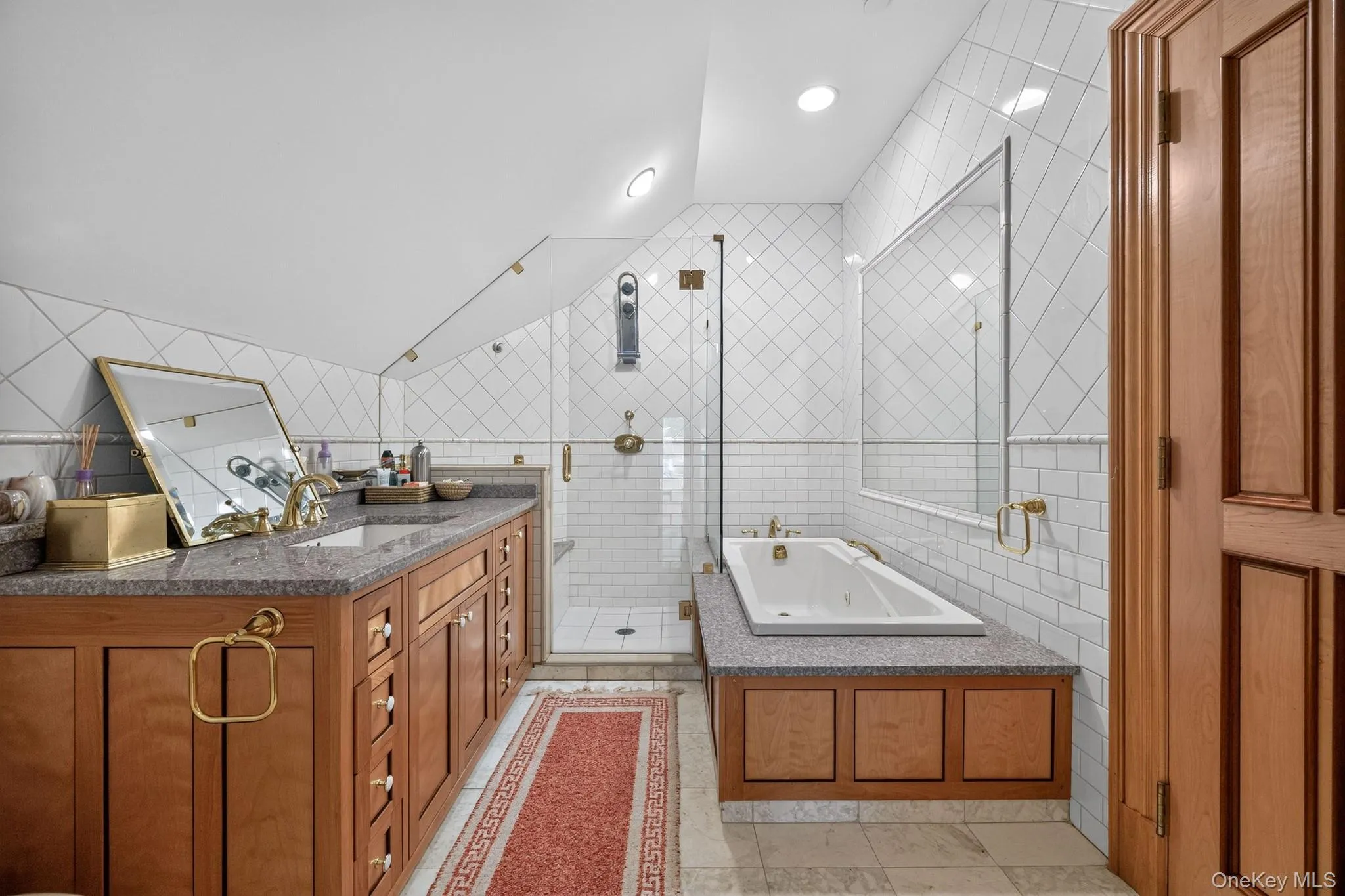 Bathroom featuring a granite-topped vanity with brass hardware, a built-in soaking tub, and a separate glass-enclosed shower with subway tile surround Bathroom featuring a granite-topped vanity with brass hardware, a built-in soaking tub, and a separate glass-enclosed shower with subway tile surround