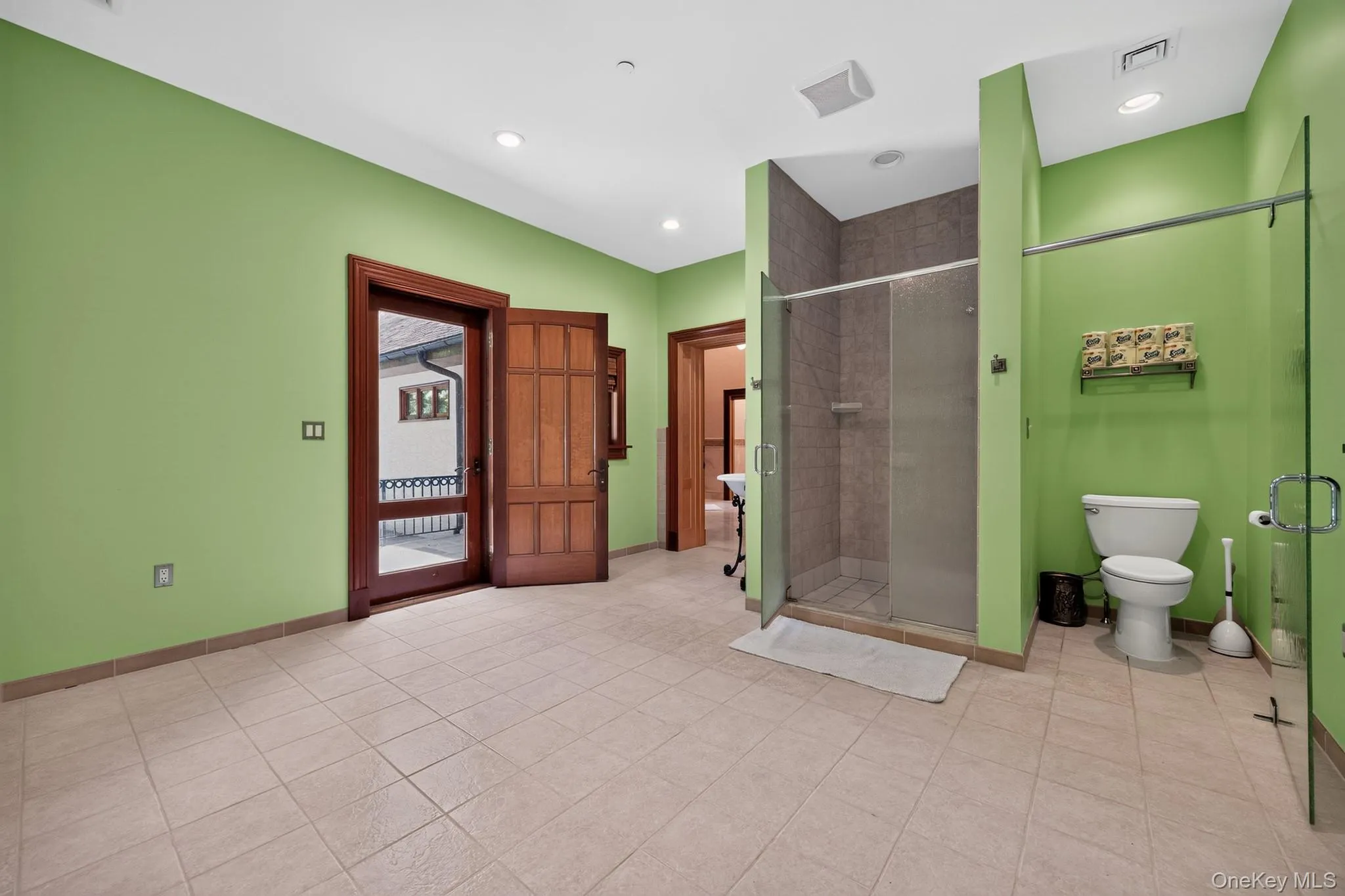 Spacious bathroom featuring tiled flooring, a glass-enclosed shower, and a private toilet area Spacious bathroom featuring tiled flooring, a glass-enclosed shower, and a private toilet area