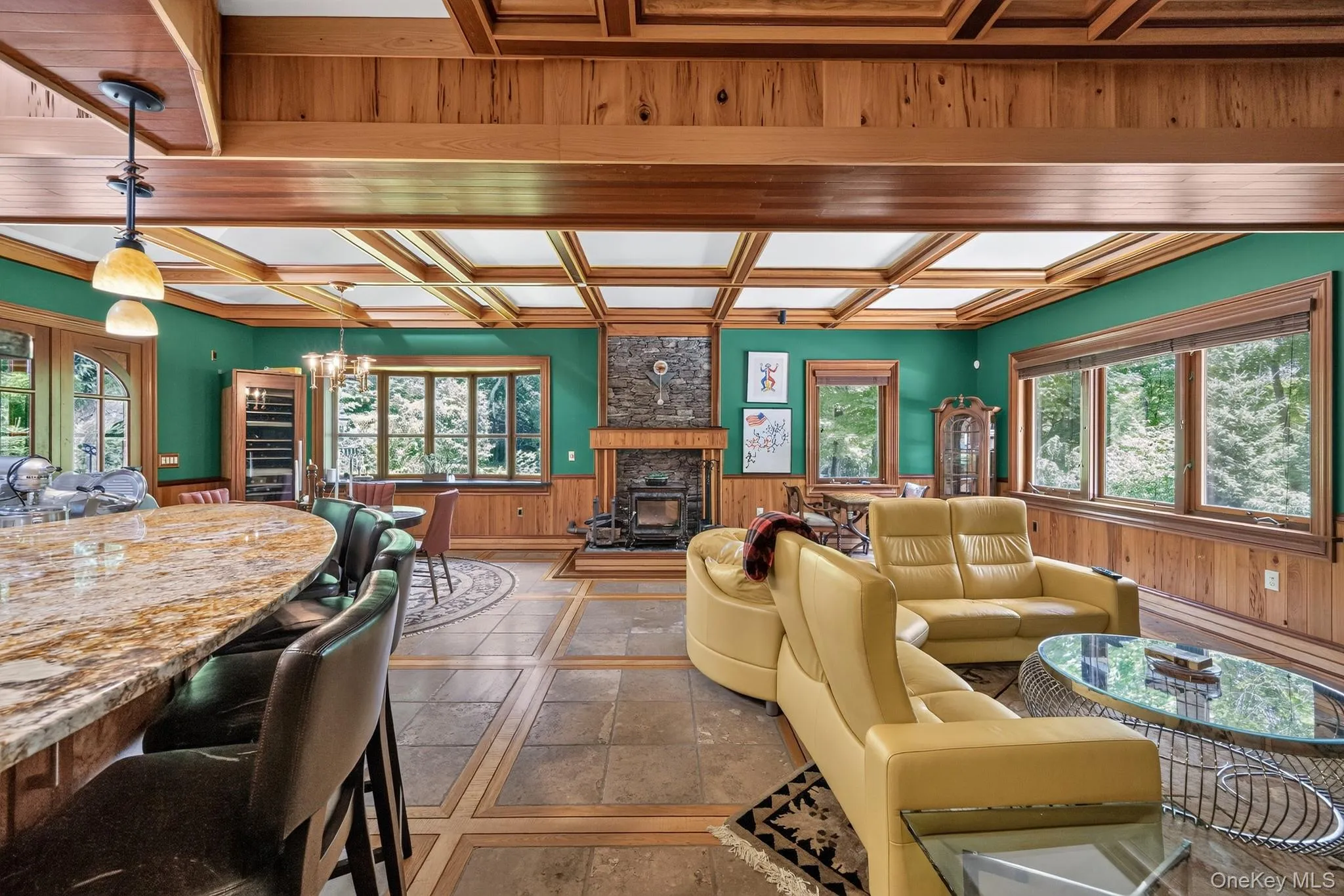 Spacious interior featuring a coffered wood ceiling, stone-surround fireplace with a wood stove, and large windows Spacious interior featuring a coffered wood ceiling, stone-surround fireplace with a wood stove, and large windows