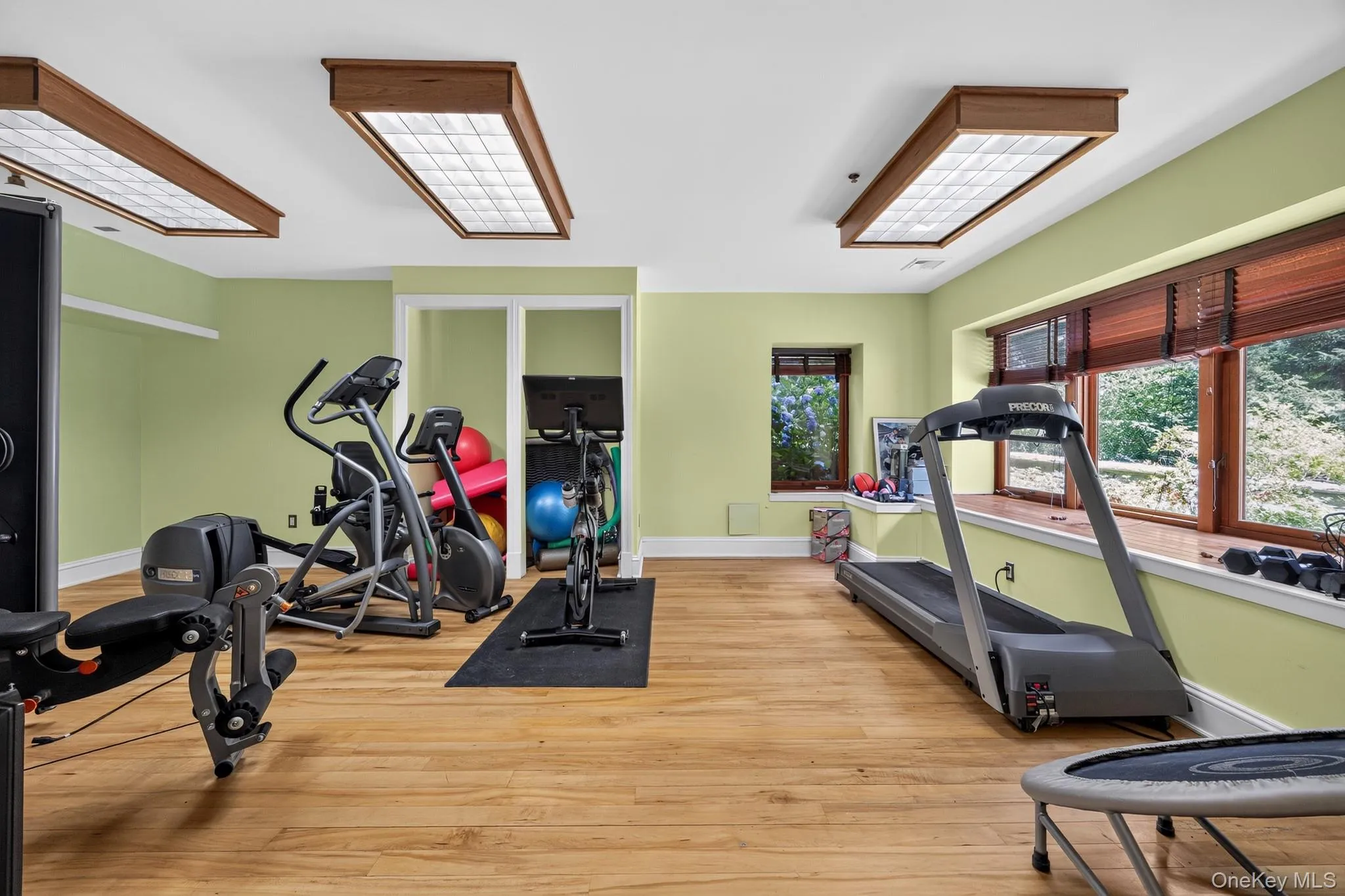 Dedicated fitness area with wood-finish flooring, two large recessed ceiling light fixtures, built-in window seating, and multiple windows with wood blinds Dedicated fitness area with wood-finish flooring, two large recessed ceiling light fixtures, built-in window seating, and multiple windows with wood blinds