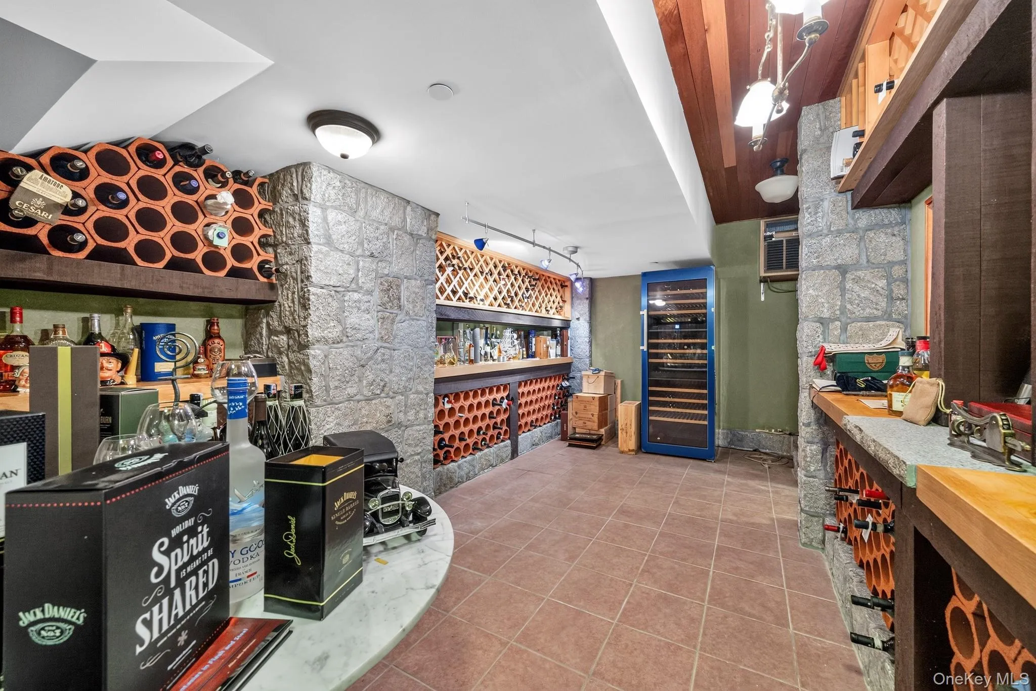 Dedicated wine storage room featuring extensive terracotta and wood-finish bottle racks, stone accent walls, a built-in bar area with a solid surface countertop, and tiled flooring Dedicated wine storage room featuring extensive terracotta and wood-finish bottle racks, stone accent walls, a built-in bar area with a solid surface countertop, and tiled flooring