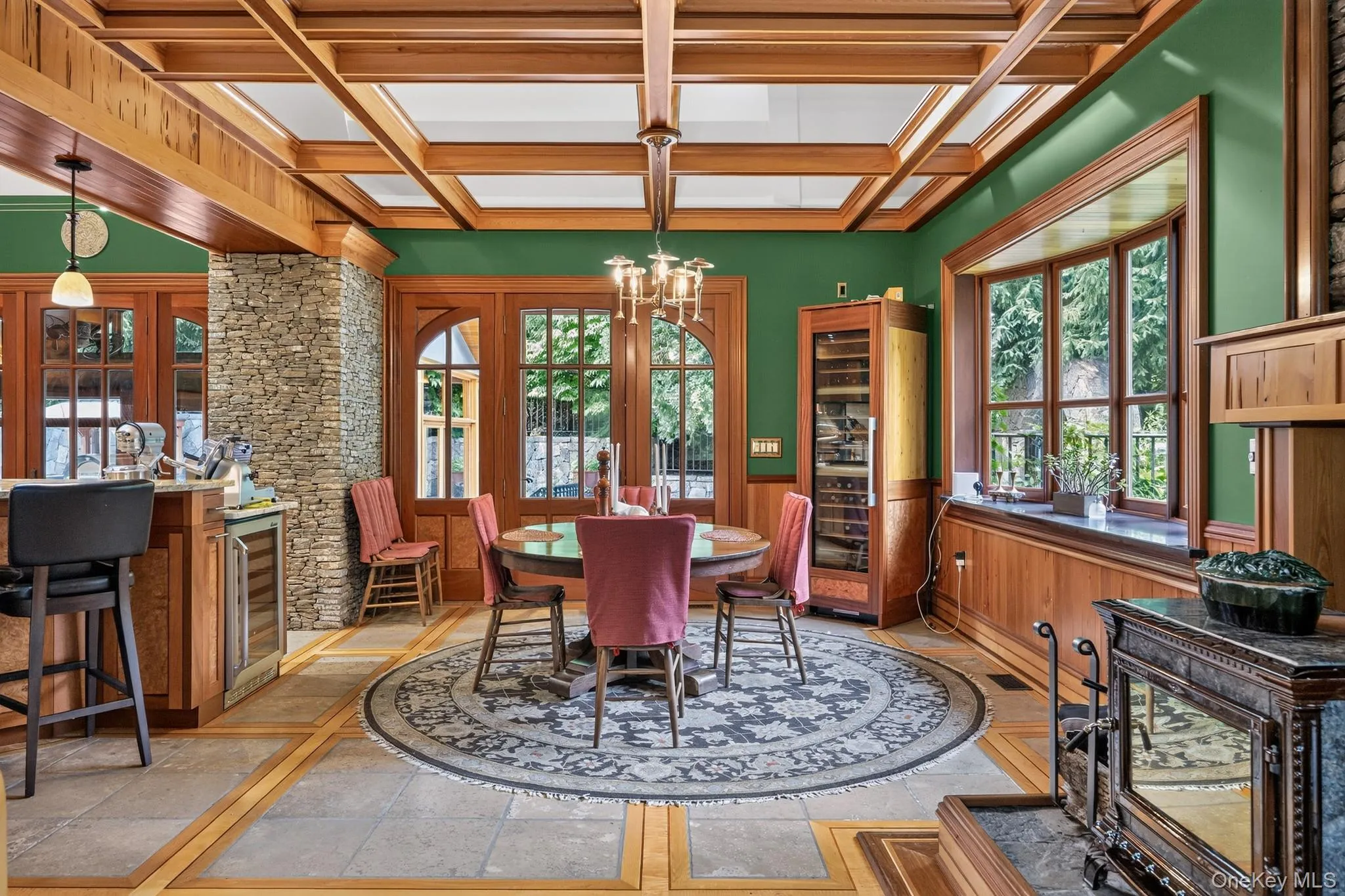 Spacious interior featuring a coffered wood ceiling, stone veneer column, built-in wine refrigeration, and large wood-framed windows Spacious interior featuring a coffered wood ceiling, stone veneer column, built-in wine refrigeration, and large wood-framed windows