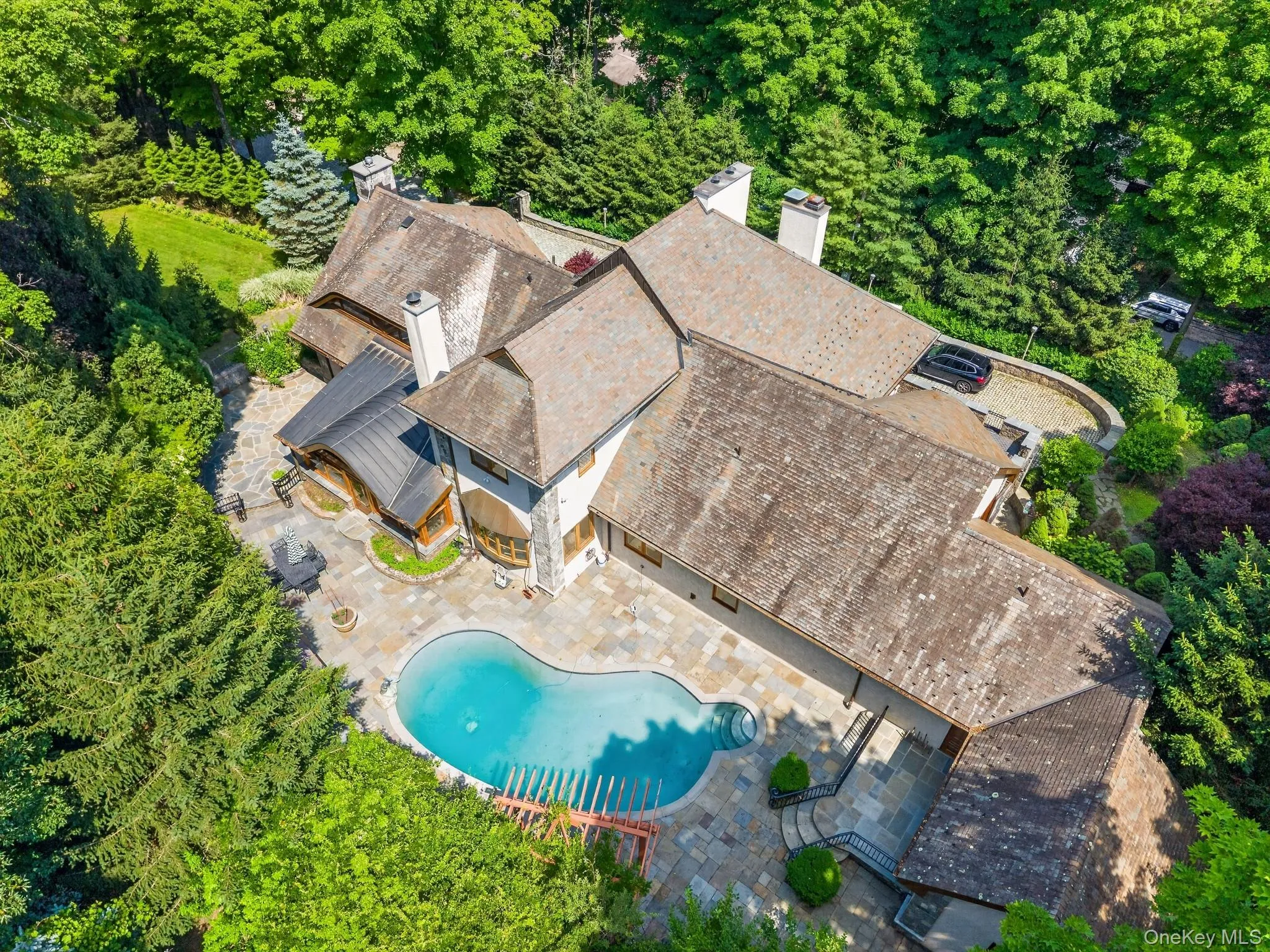 Large property featuring a freeform swimming pool with integrated spa, extensive stone patio surround, and multiple gabled rooflines Large property featuring a freeform swimming pool with integrated spa, extensive stone patio surround, and multiple gabled rooflines