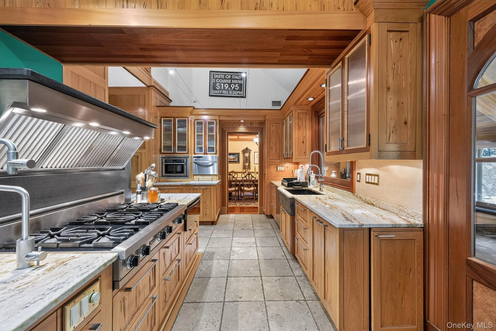 Gourmet kitchen featuring a commercial-grade range with a stainless steel vent hood, extensive wood cabinetry, stone countertops, and tile flooring Gourmet kitchen featuring a commercial-grade range with a stainless steel vent hood, extensive wood cabinetry, stone countertops, and tile flooring