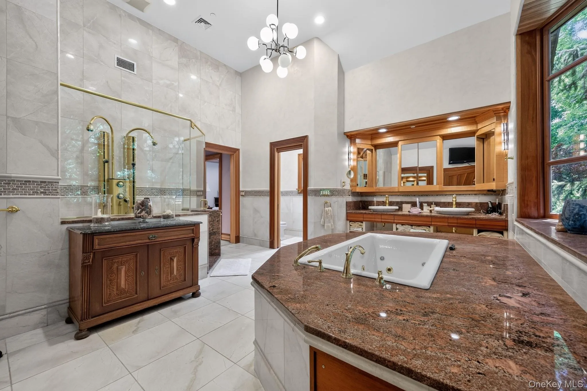 Spacious bathroom featuring a built-in jetted tub with a granite surround, dual vessel sinks with gold-tone fixtures, a walk-in shower with multiple showerheads, and a large wood-framed window Spacious bathroom featuring a built-in jetted tub with a granite surround, dual vessel sinks with gold-tone fixtures, a walk-in shower with multiple showerheads, and a large wood-framed window