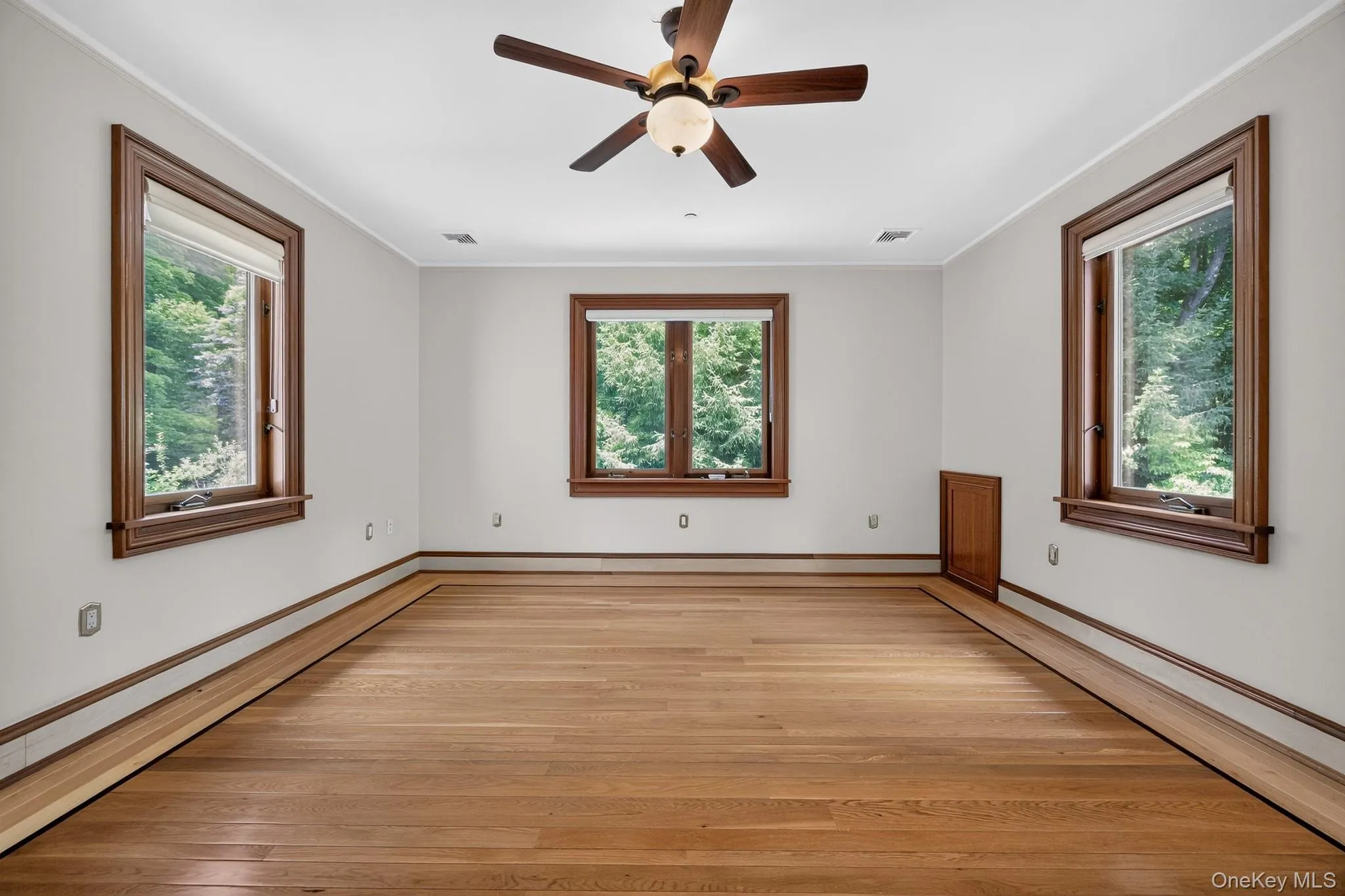 Spacious room featuring wood-finish flooring, white walls, and a ceiling fan with integrated lighting Spacious room featuring wood-finish flooring, white walls, and a ceiling fan with integrated lighting