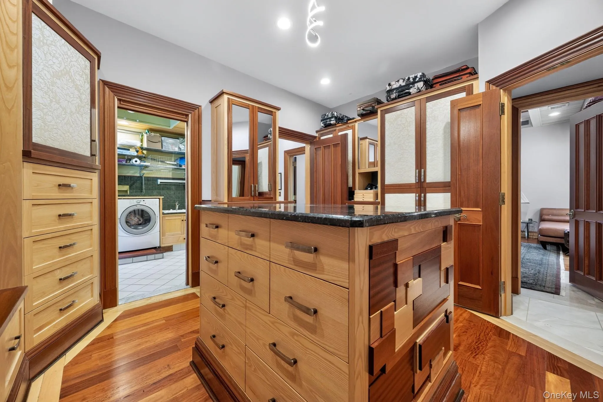 Walk-in closet featuring a central island with a dark countertop and multiple drawers Walk-in closet featuring a central island with a dark countertop and multiple drawers