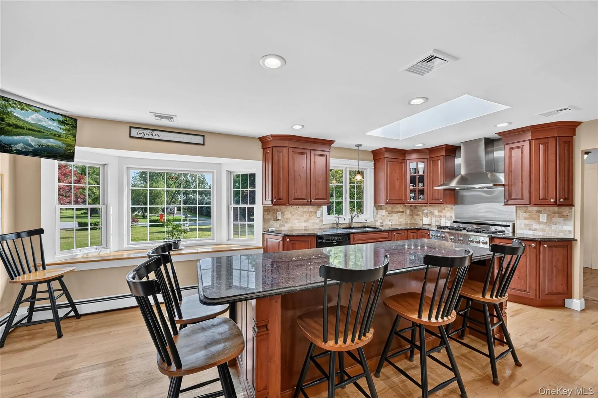 Natural light pours in through the skylight and large bay window, bringing warmth to the kitchen’s rich cabinetry, granite counters, and comfortable gathering space. Natural light pours in through the skylight and large bay window, bringing warmth to the kitchen’s rich cabinetry, granite counters, and comfortable gathering space.