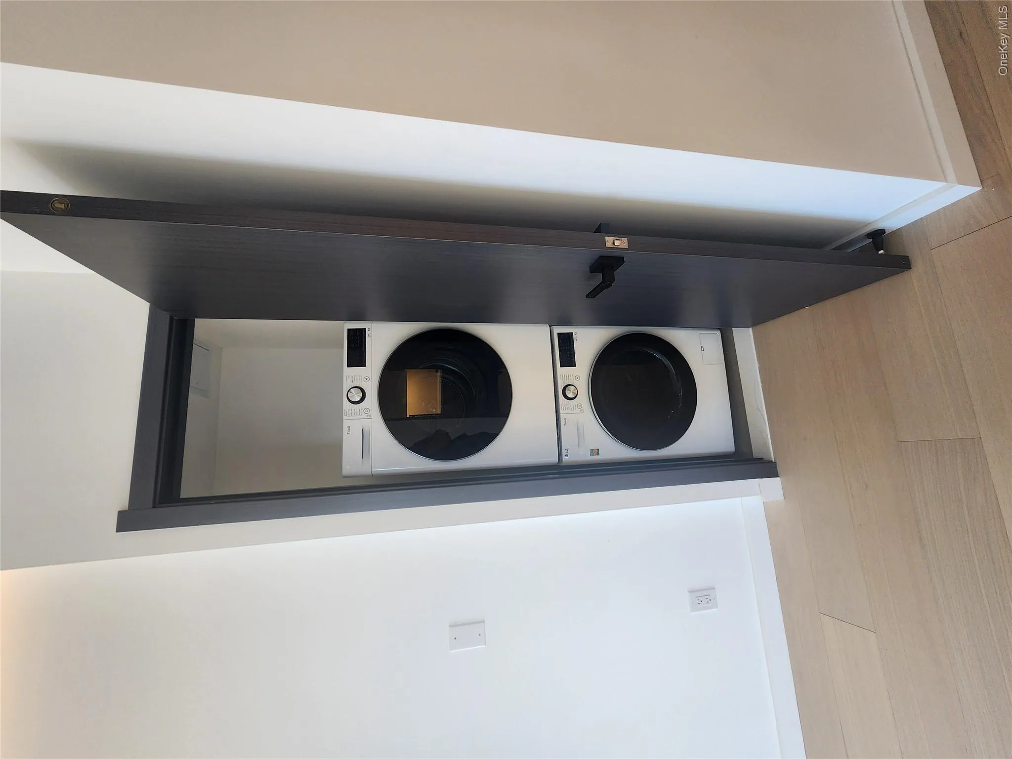 Dedicated laundry closet featuring a stacked washer and dryer unit, dark wood-finish door, and light wood-finish flooring Dedicated laundry closet featuring a stacked washer and dryer unit, dark wood-finish door, and light wood-finish flooring