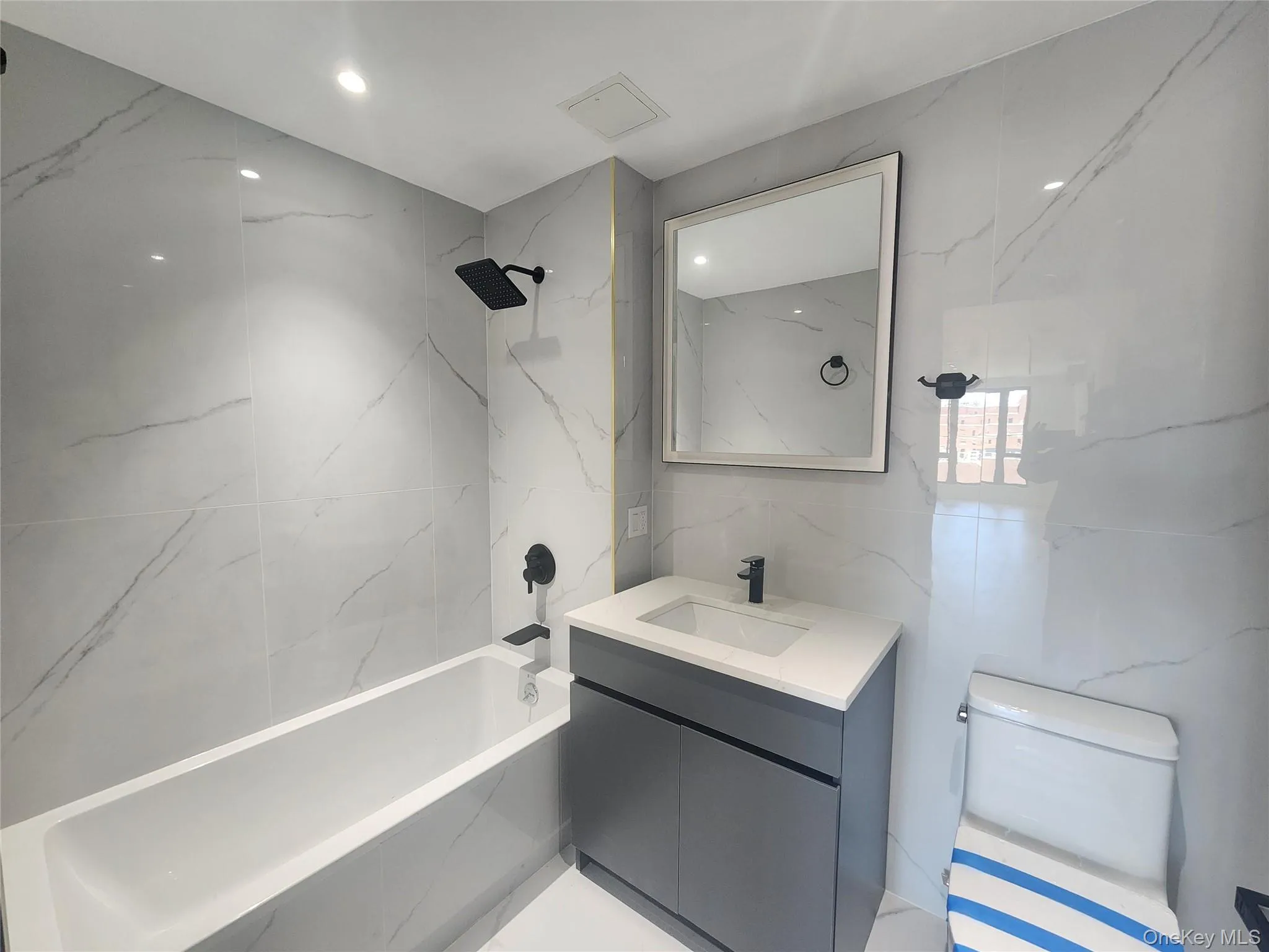 Contemporary bathroom featuring large format wall tiles with subtle veining, recessed lighting, and a white soaking tub with matte black fixtures Contemporary bathroom featuring large format wall tiles with subtle veining, recessed lighting, and a white soaking tub with matte black fixtures