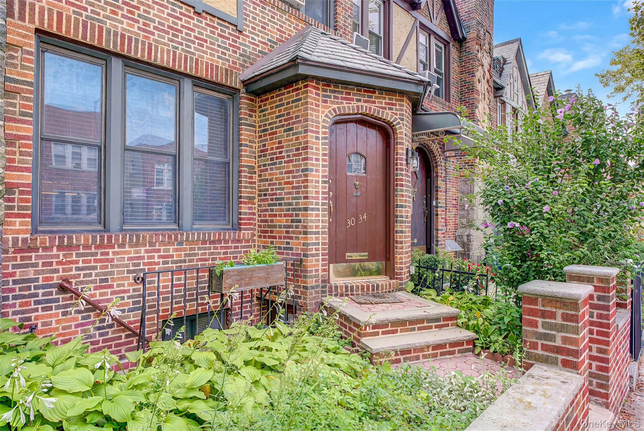 Brick facade with arched entry door, sheltered by an overhang, featuring stone steps and wrought iron railings Brick facade with arched entry door, sheltered by an overhang, featuring stone steps and wrought iron railings