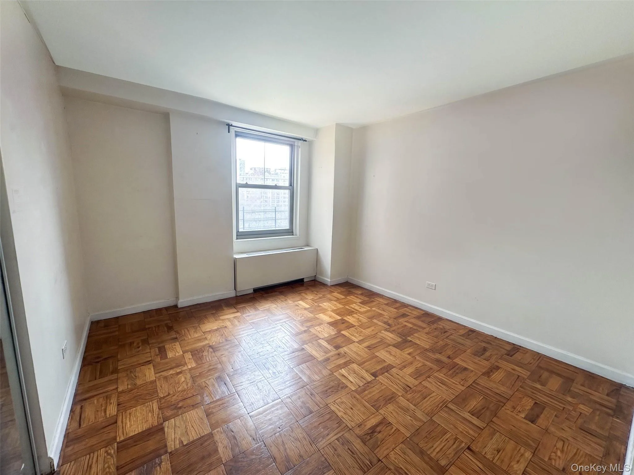 Room featuring wood parquet flooring, a large window, white walls, and white baseboards Room featuring wood parquet flooring, a large window, white walls, and white baseboards