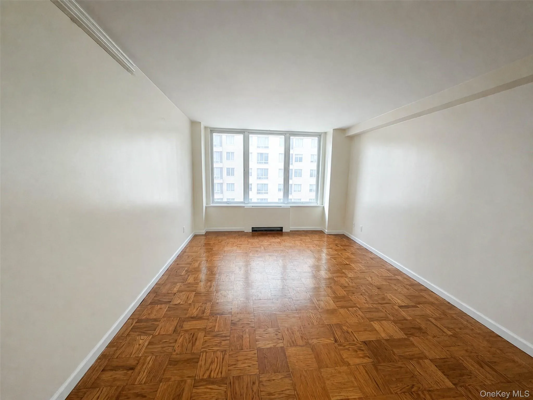 Spacious room featuring parquet wood flooring, white baseboards, and light-colored walls Spacious room featuring parquet wood flooring, white baseboards, and light-colored walls