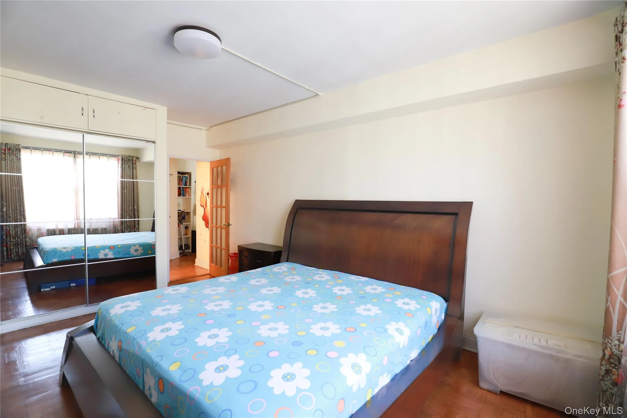 Bedroom featuring wood-finish flooring, a contemporary ceiling light fixture, and a built-in wardrobe with mirrored sliding doors Bedroom featuring wood-finish flooring, a contemporary ceiling light fixture, and a built-in wardrobe with mirrored sliding doors
