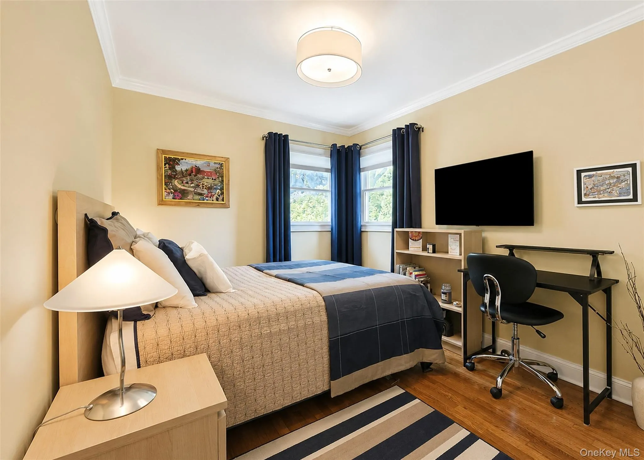 Bedroom featuring wood-finish flooring, crown molding, and two windows with natural light Bedroom featuring wood-finish flooring, crown molding, and two windows with natural light