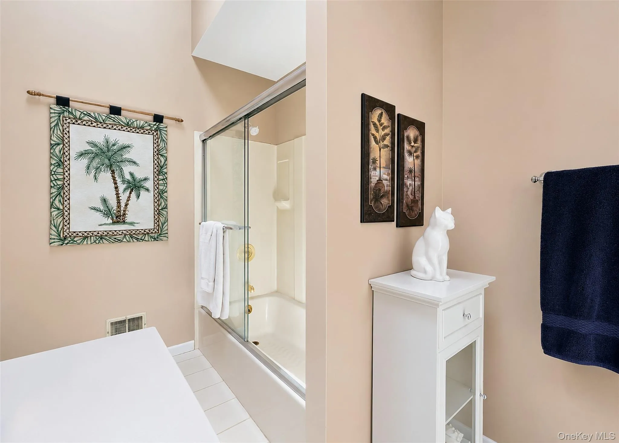 Bathroom featuring a tub and shower combination with a sliding glass enclosure, light-toned wall paint, and white tile flooring Bathroom featuring a tub and shower combination with a sliding glass enclosure, light-toned wall paint, and white tile flooring