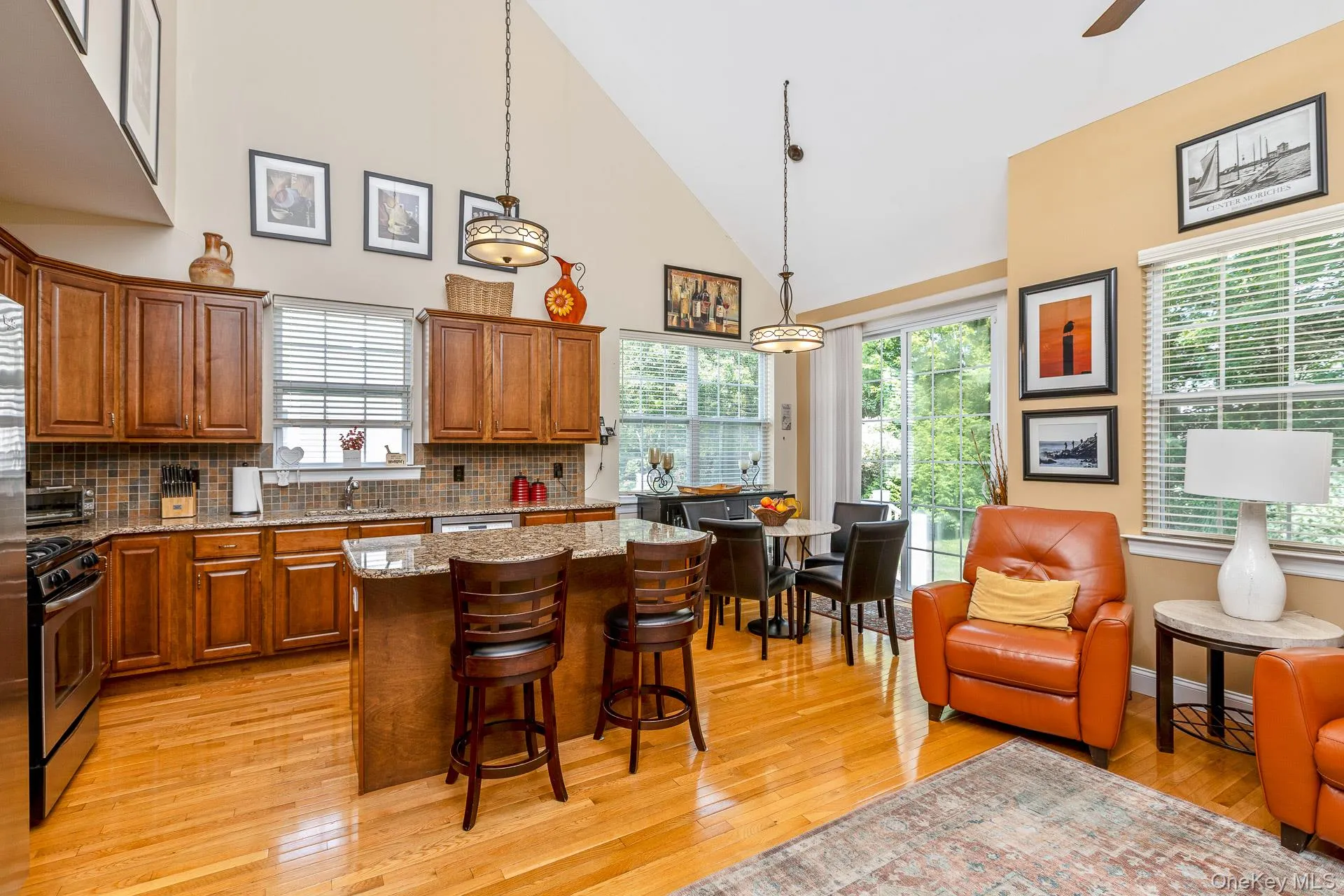 Open-concept Kitchen featuring vaulted ceilings, wood-finish flooring, a large island with seating, stainless steel appliances, and a glass sliding door to yard Open-concept Kitchen featuring vaulted ceilings, wood-finish flooring, a large island with seating, stainless steel appliances, and a glass sliding door to yard